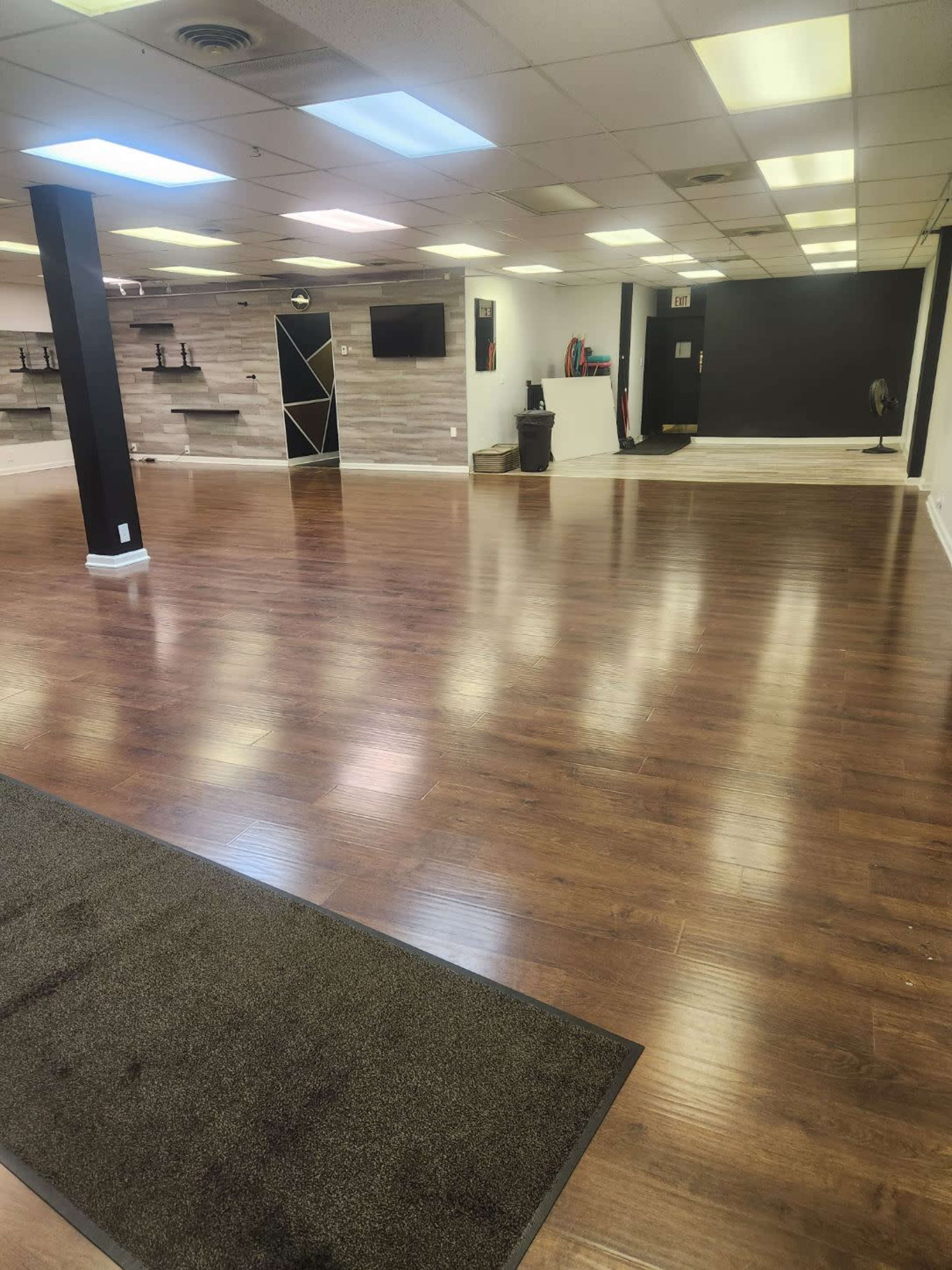 An empty commercial space with hardwood flooring, white walls, and several overhead lights.