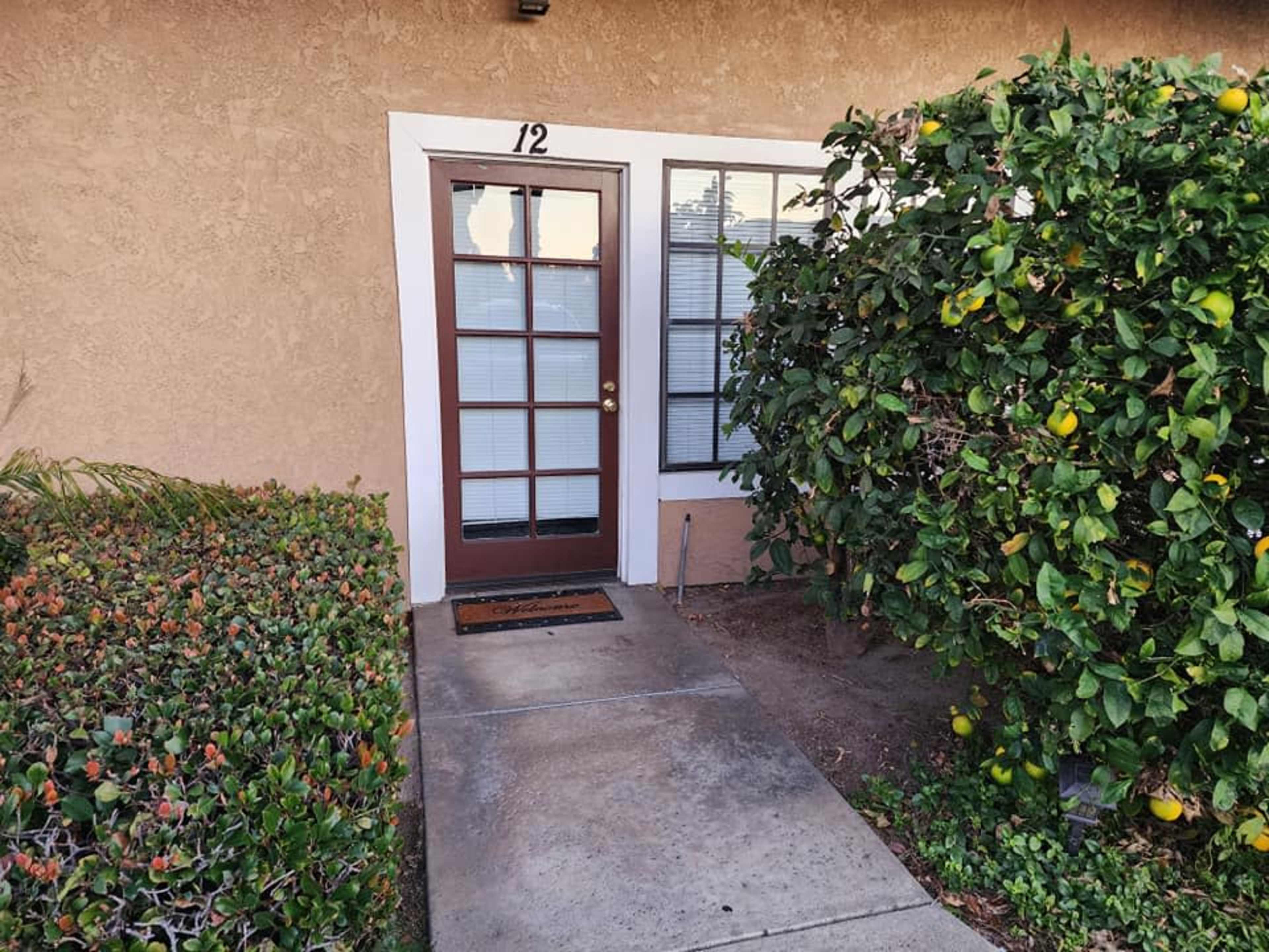 The entrance of a unit marked "12," with a shrub on one side and a manicured path leading to the door.