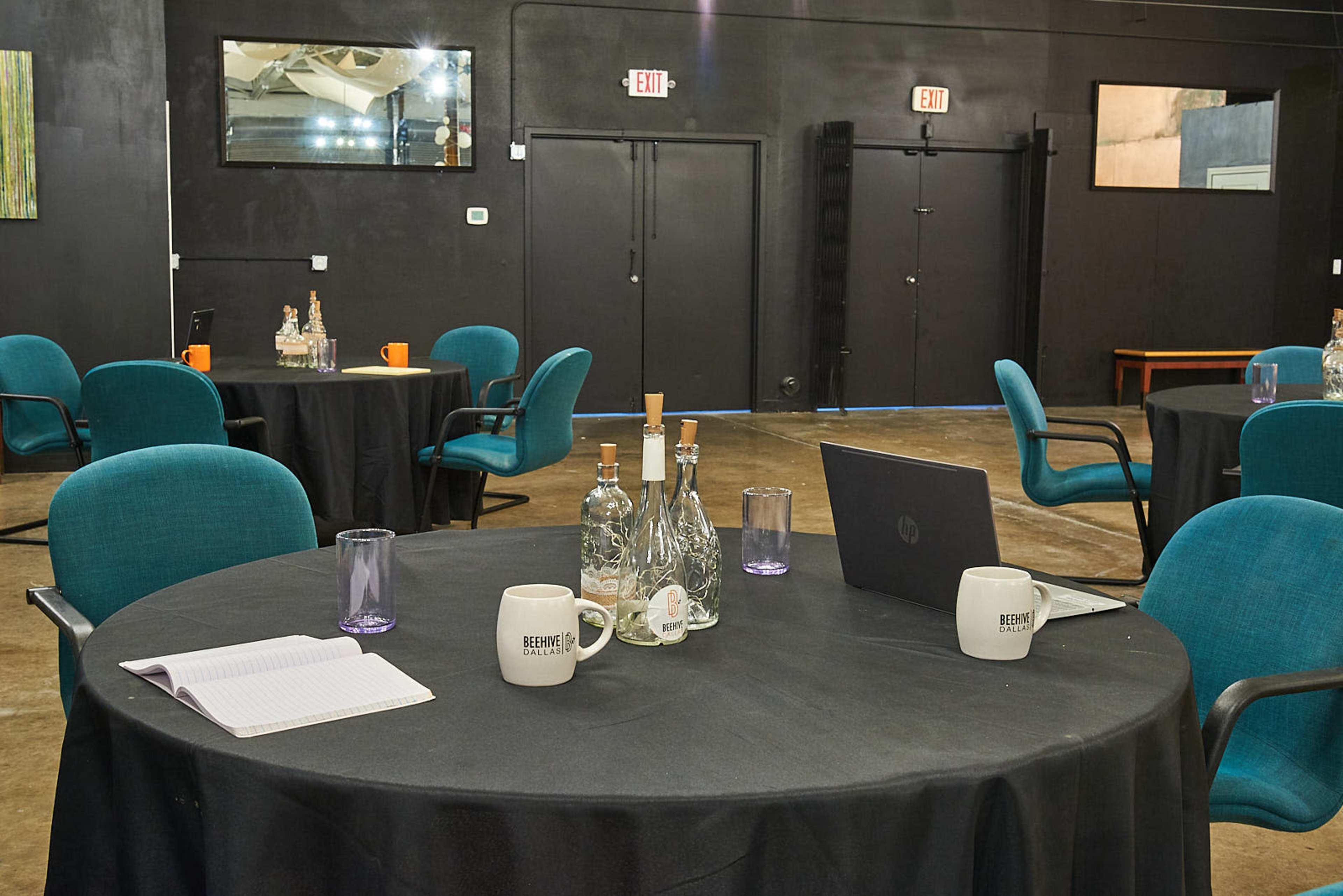 A conference room with round tables covered in black tablecloths, each equipped with chairs, bottles of water, and notebooks, all set for a meeting.