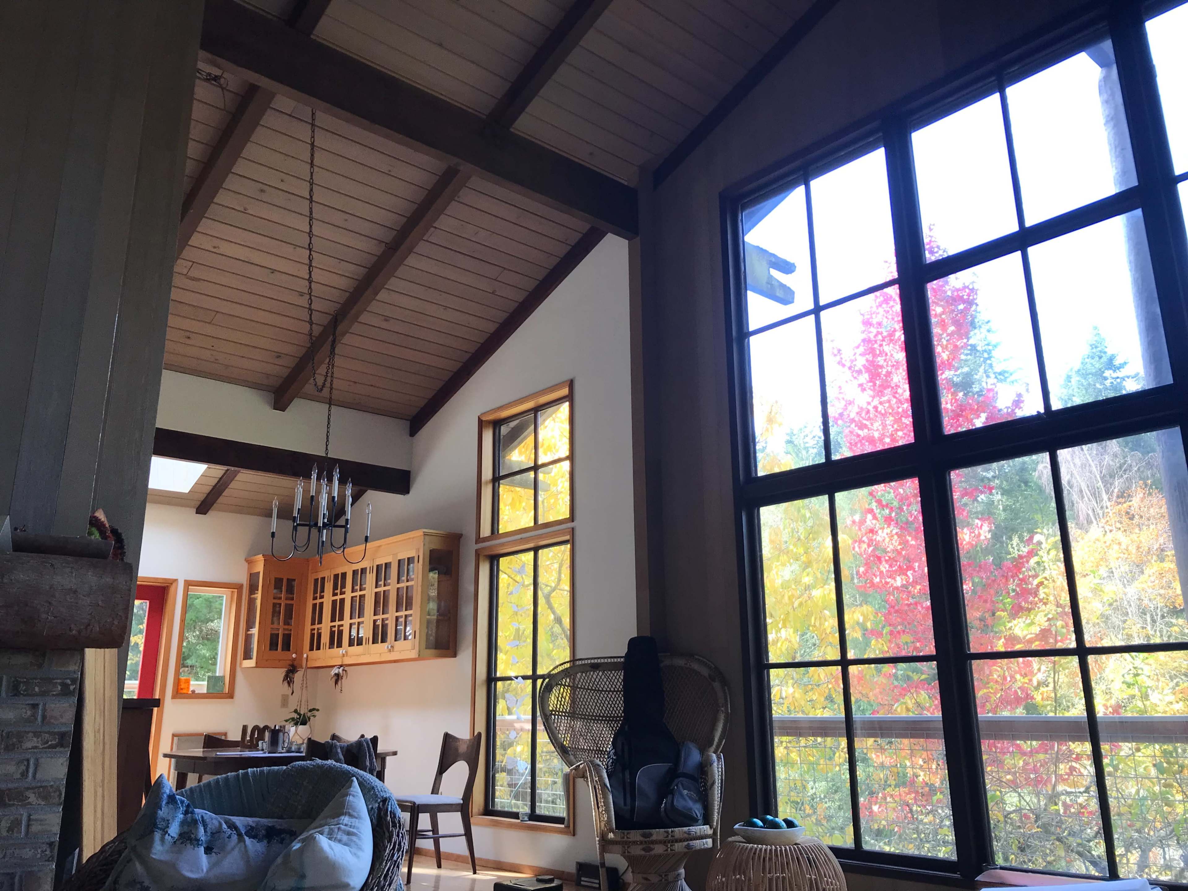 A brightly lit room features large windows with a view of colorful autumn trees, wooden beams, and a cozy seating area.