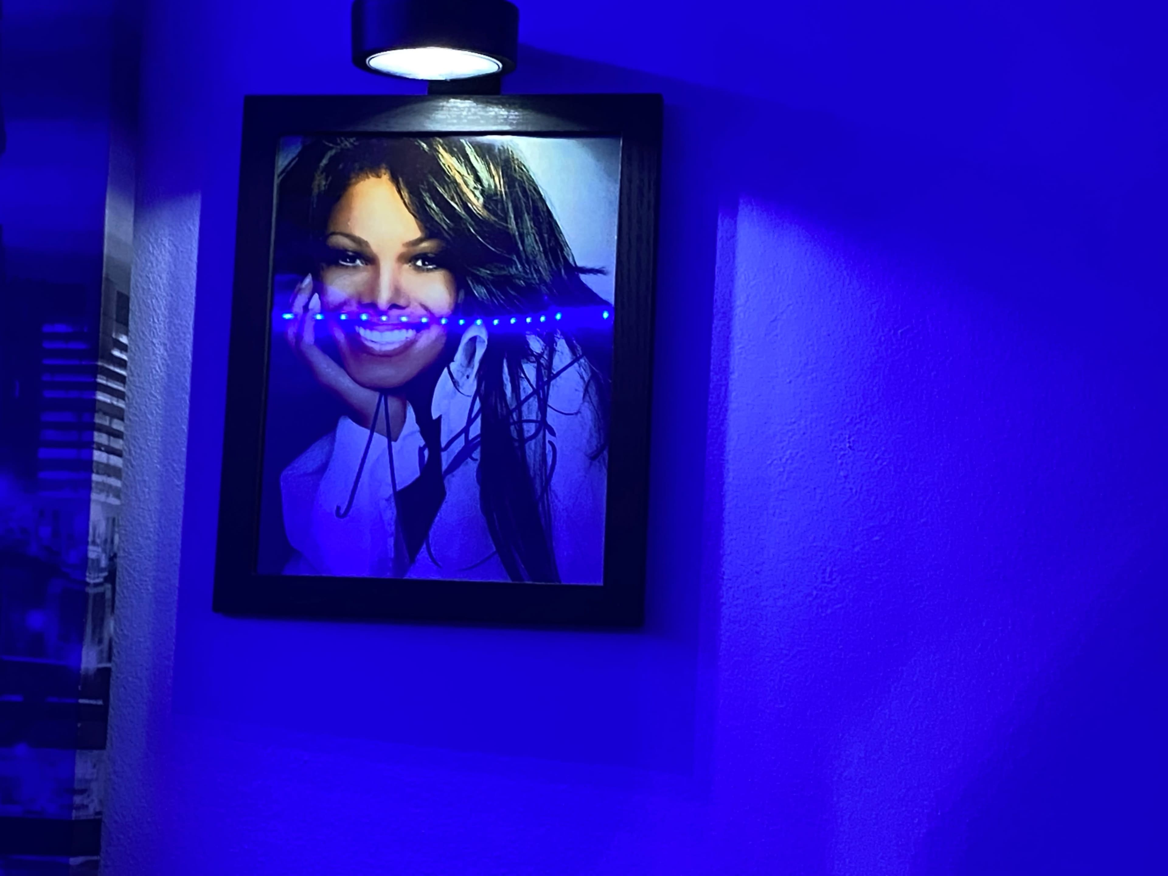 A framed photograph of a smiling woman on a wall, illuminated by a blue light.