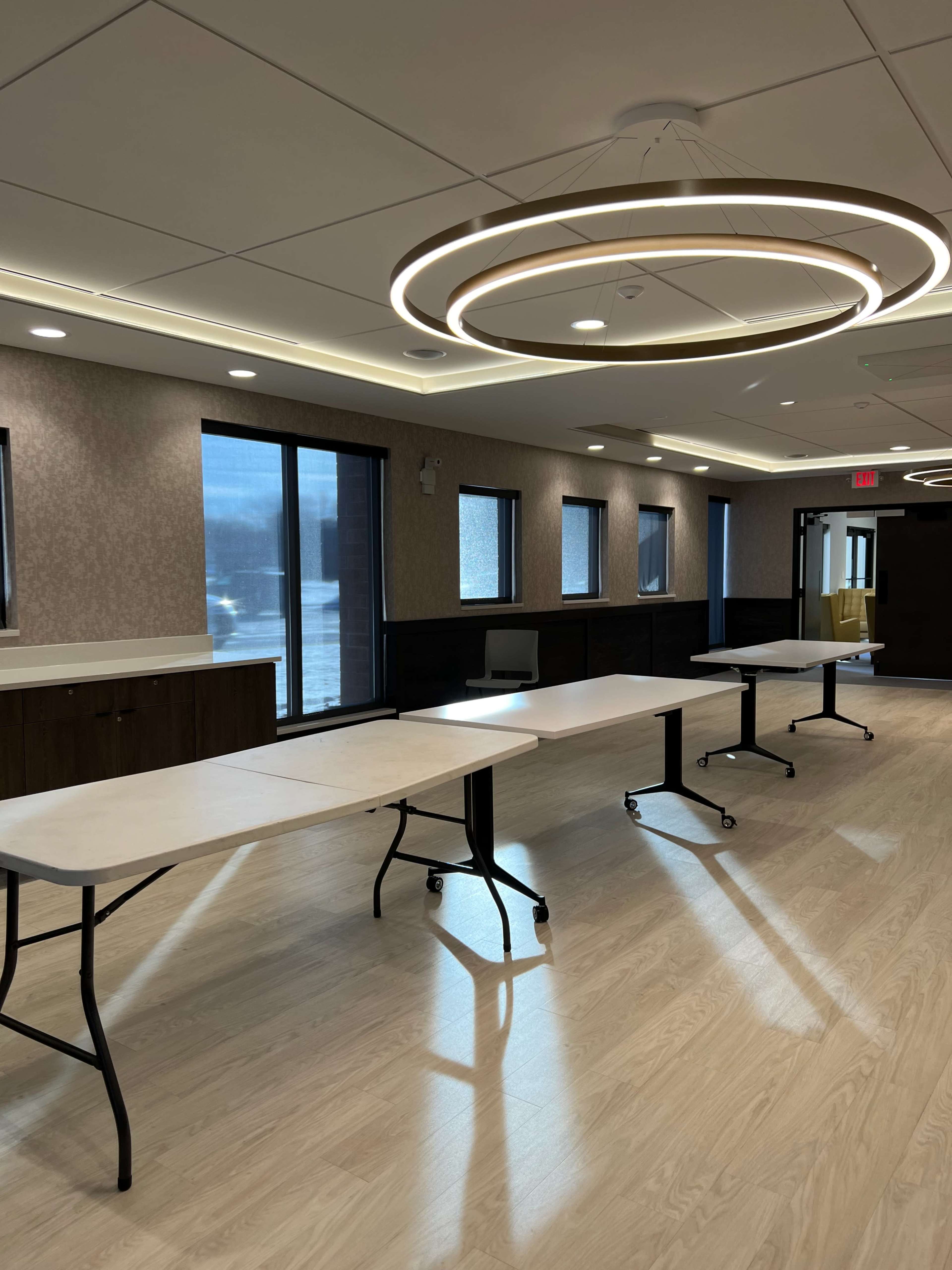 A modern room with several folding tables arranged in a row, accompanied by large windows that allow natural light to enter.