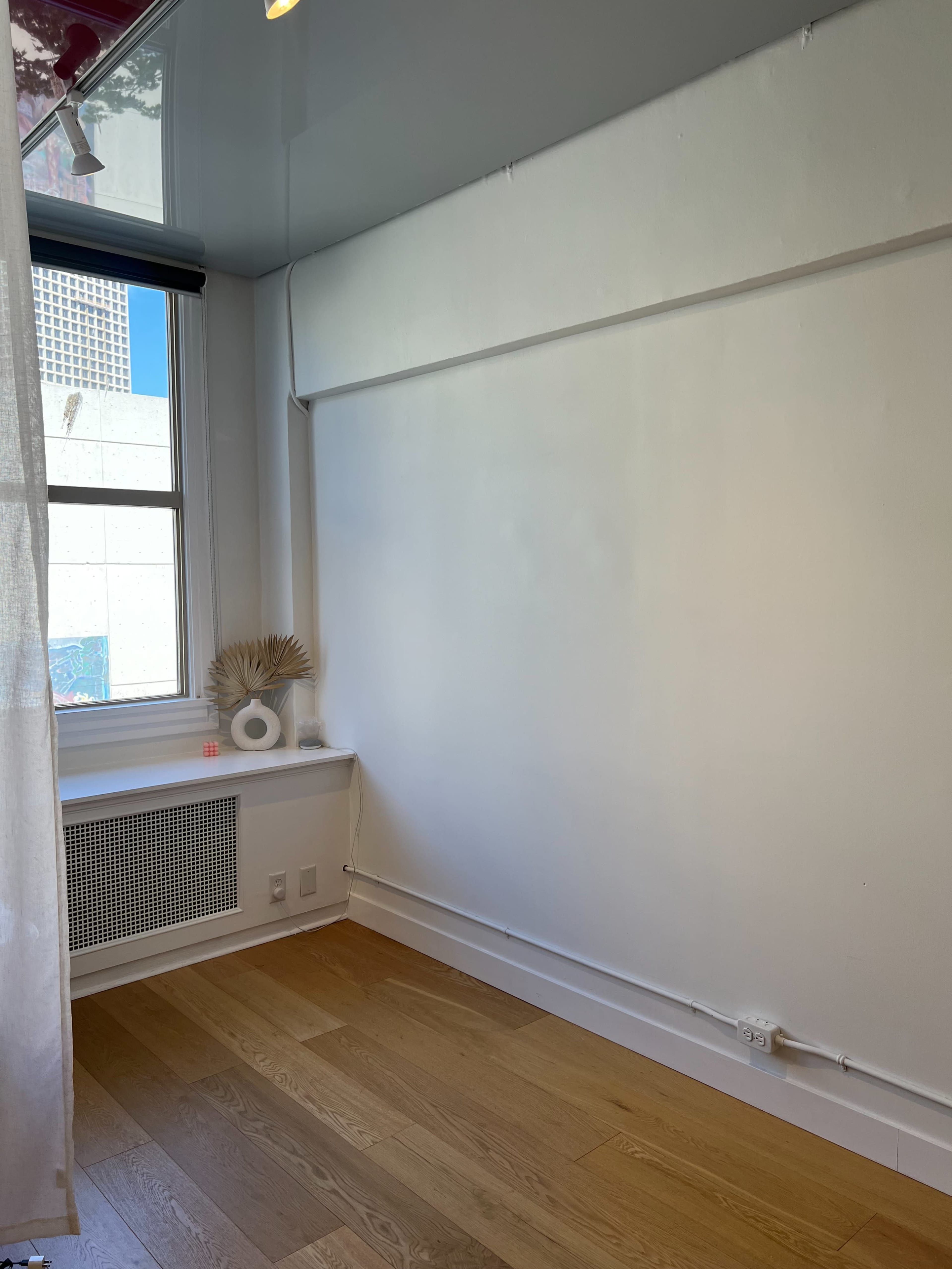 A minimalistic room with a large window, white walls, and a wooden floor, featuring a small decorative arrangement on the window sill.