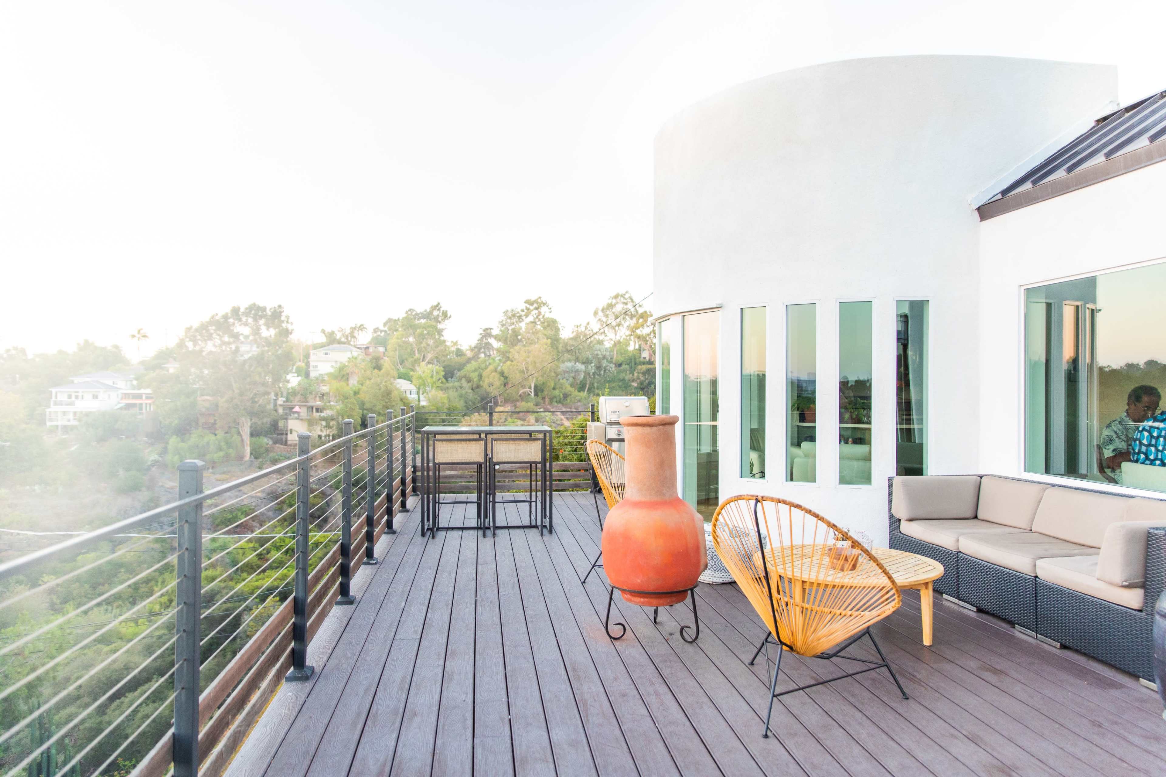 A modern rooftop terrace features a seating area, a large clay pot, and views of surrounding greenery.