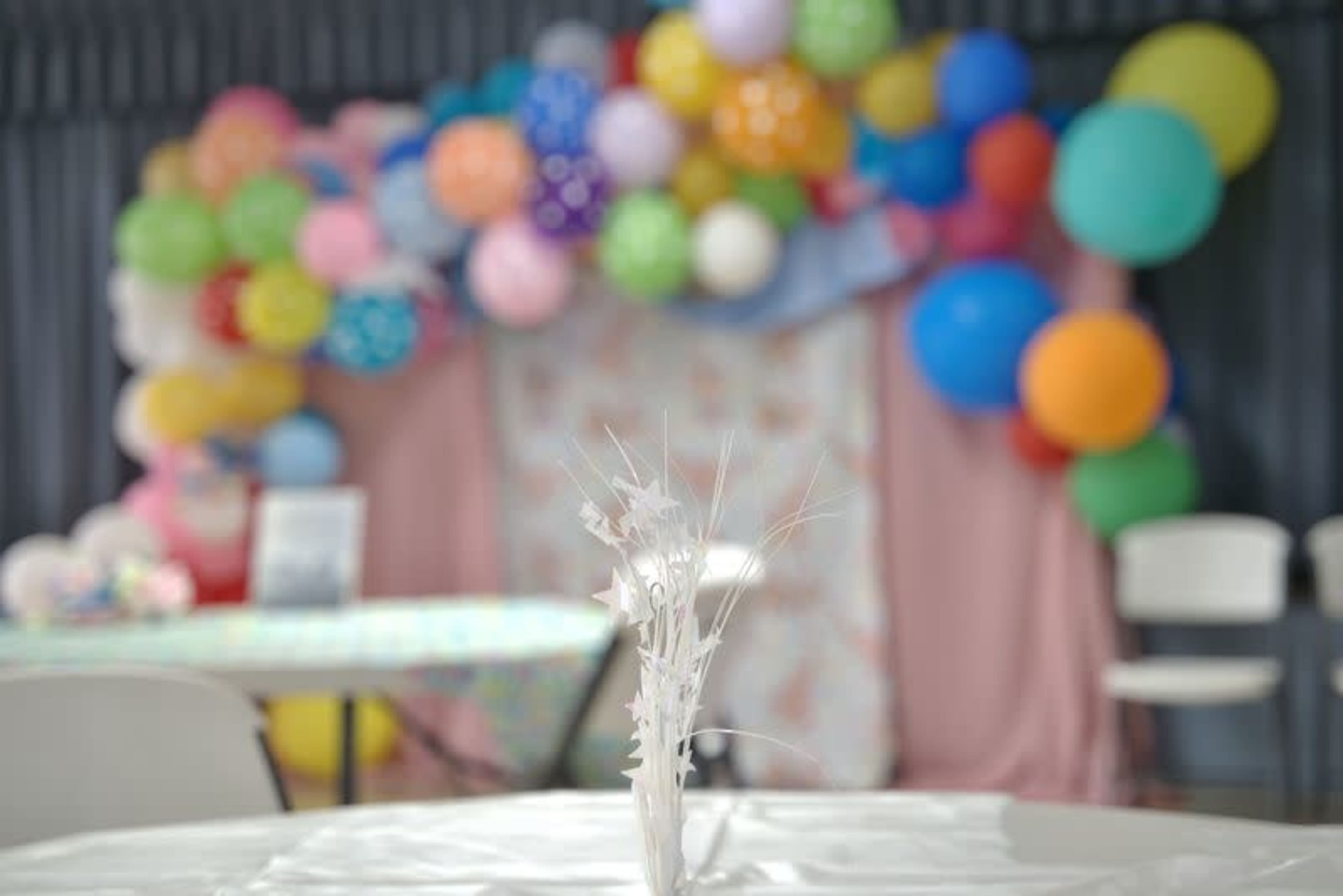 A table with a decorative centerpiece is positioned in front of a colorful backdrop made of balloons.