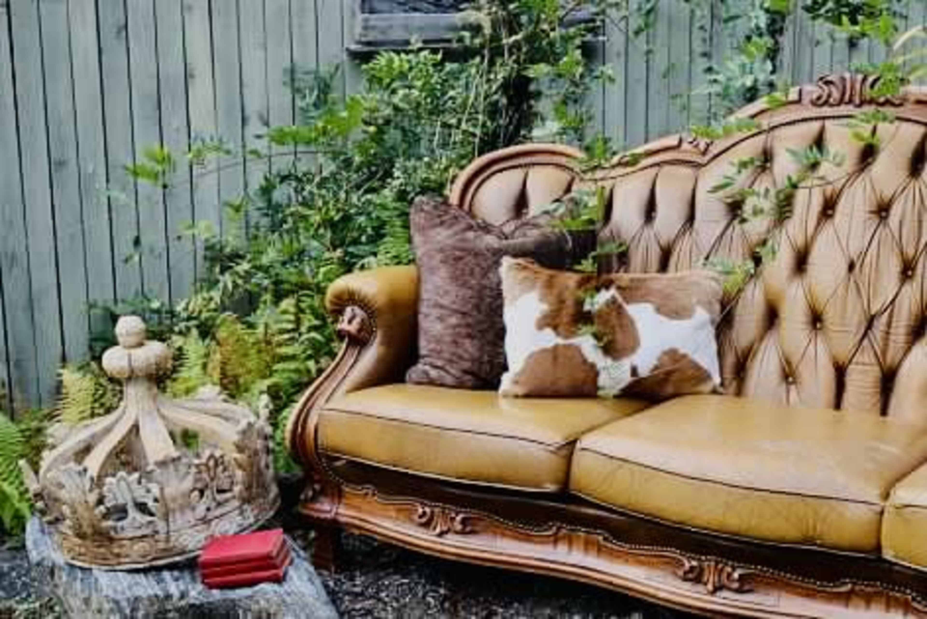 A yellow tufted sofa is placed next to a crown-shaped sculpture and surrounded by greenery.