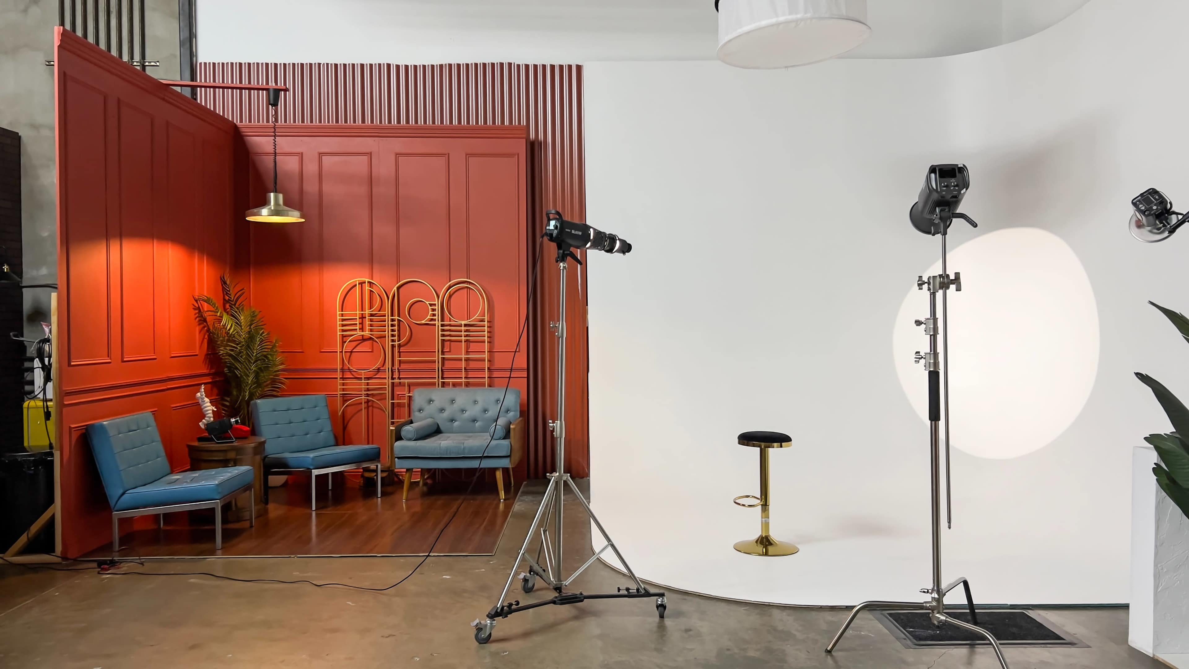 The image shows a photography studio setup featuring a red-paneled section with blue seating and a white backdrop with lighting equipment.