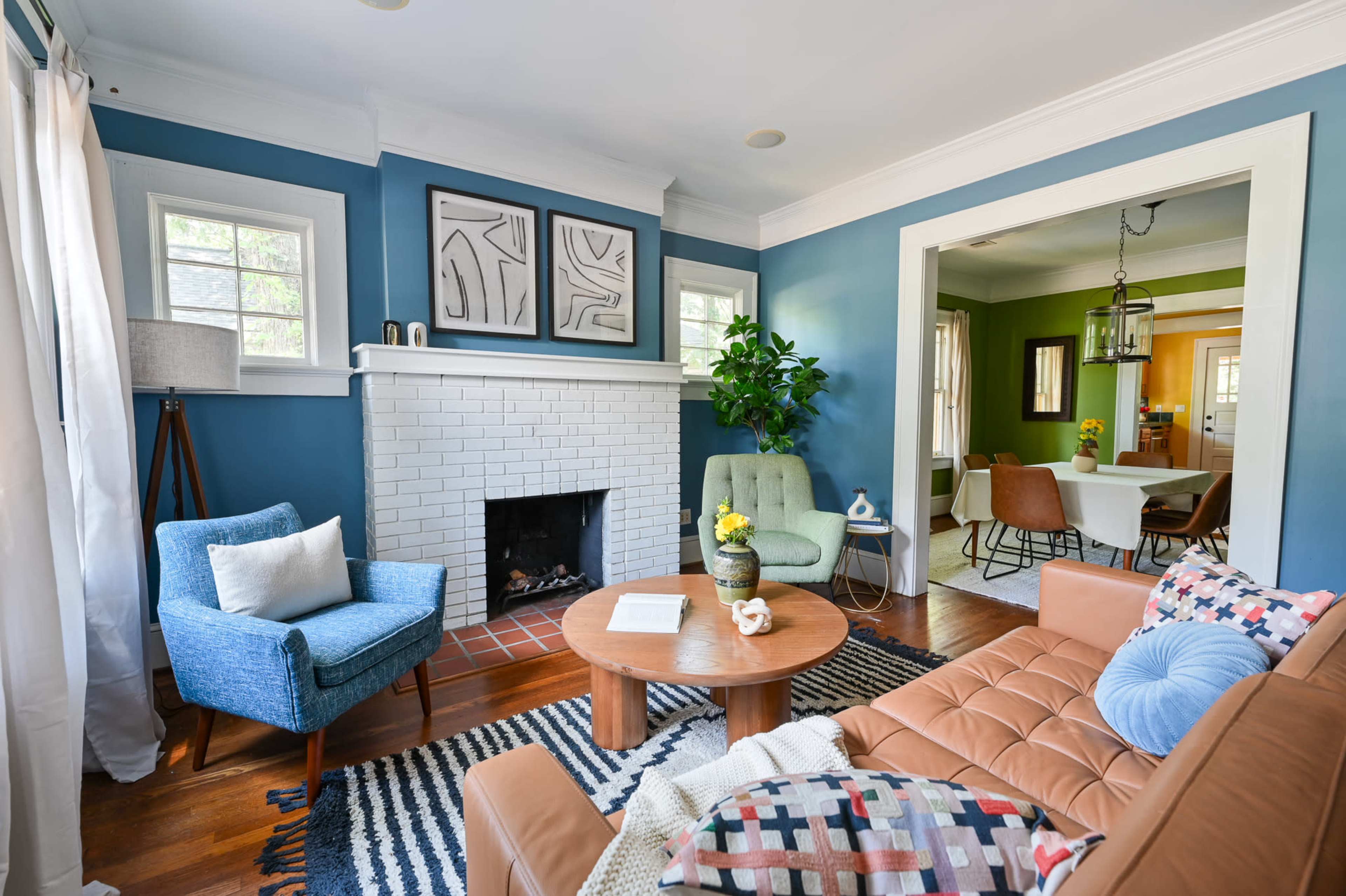 A cozy living room with a brown leather sofa, blue accent chairs, a round coffee table, and a white brick fireplace surrounded by blue walls.