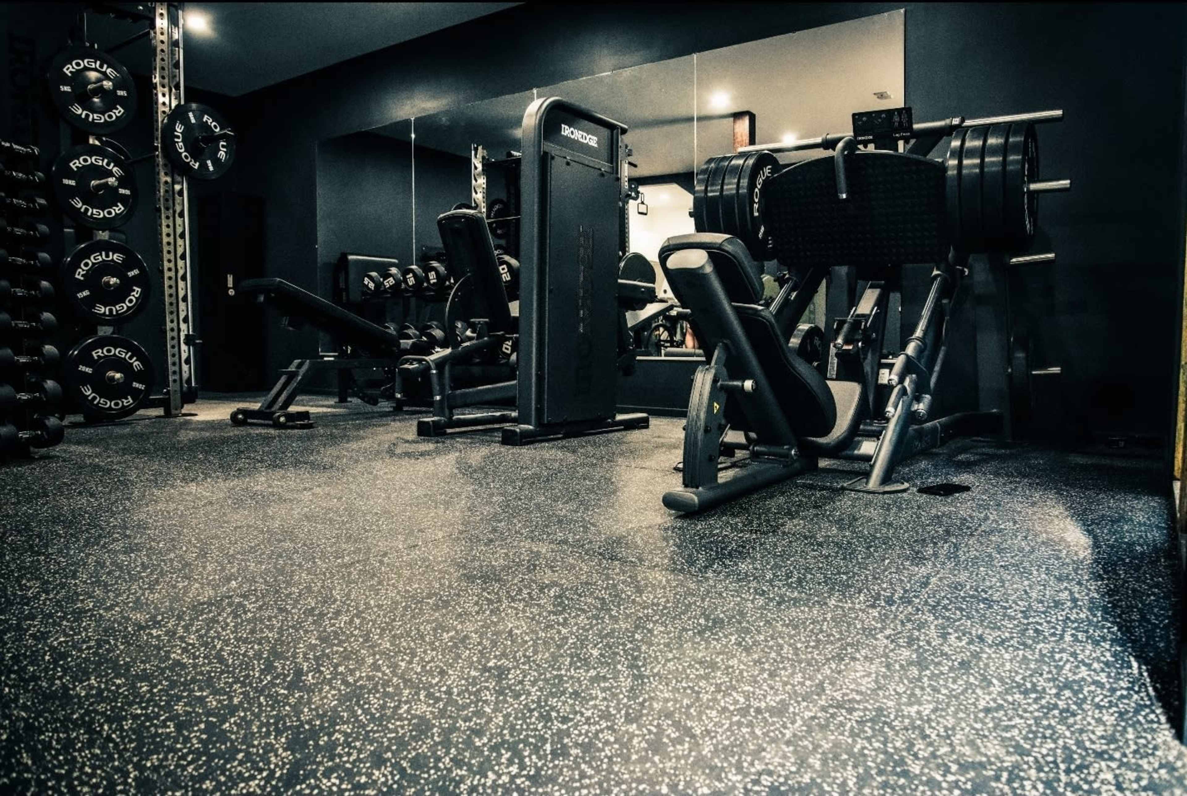 The image shows a well-equipped gym with various weightlifting machines and free weights arranged along the walls.