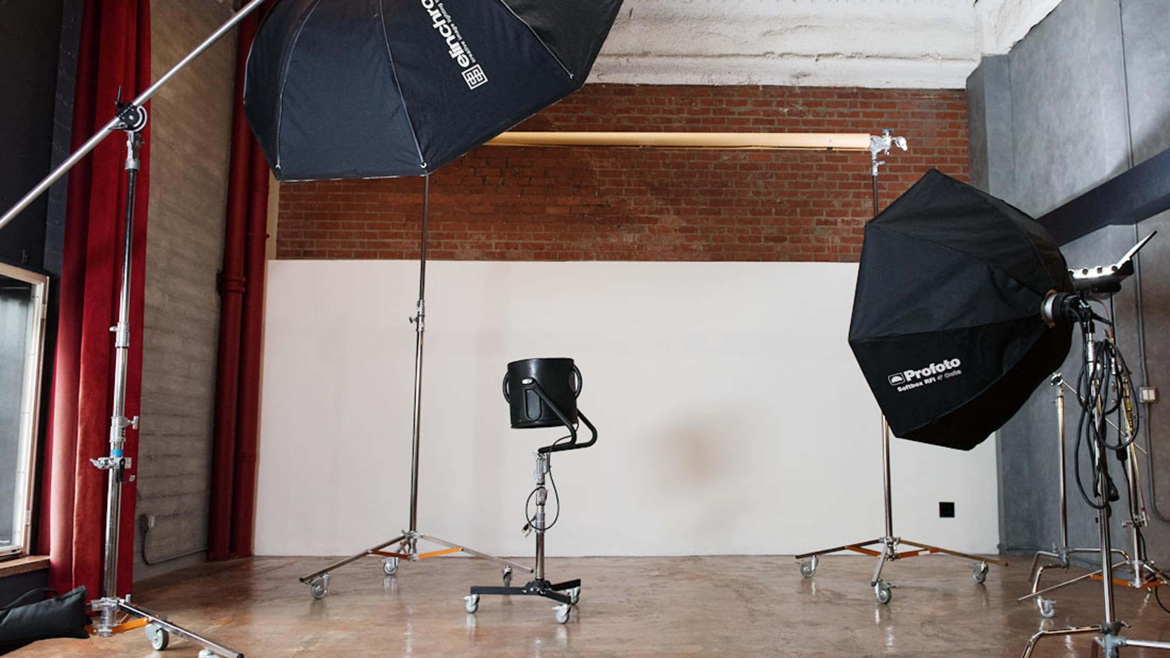 The image shows a photography studio setup with two large light softboxes, a black chair, and a plain white backdrop.