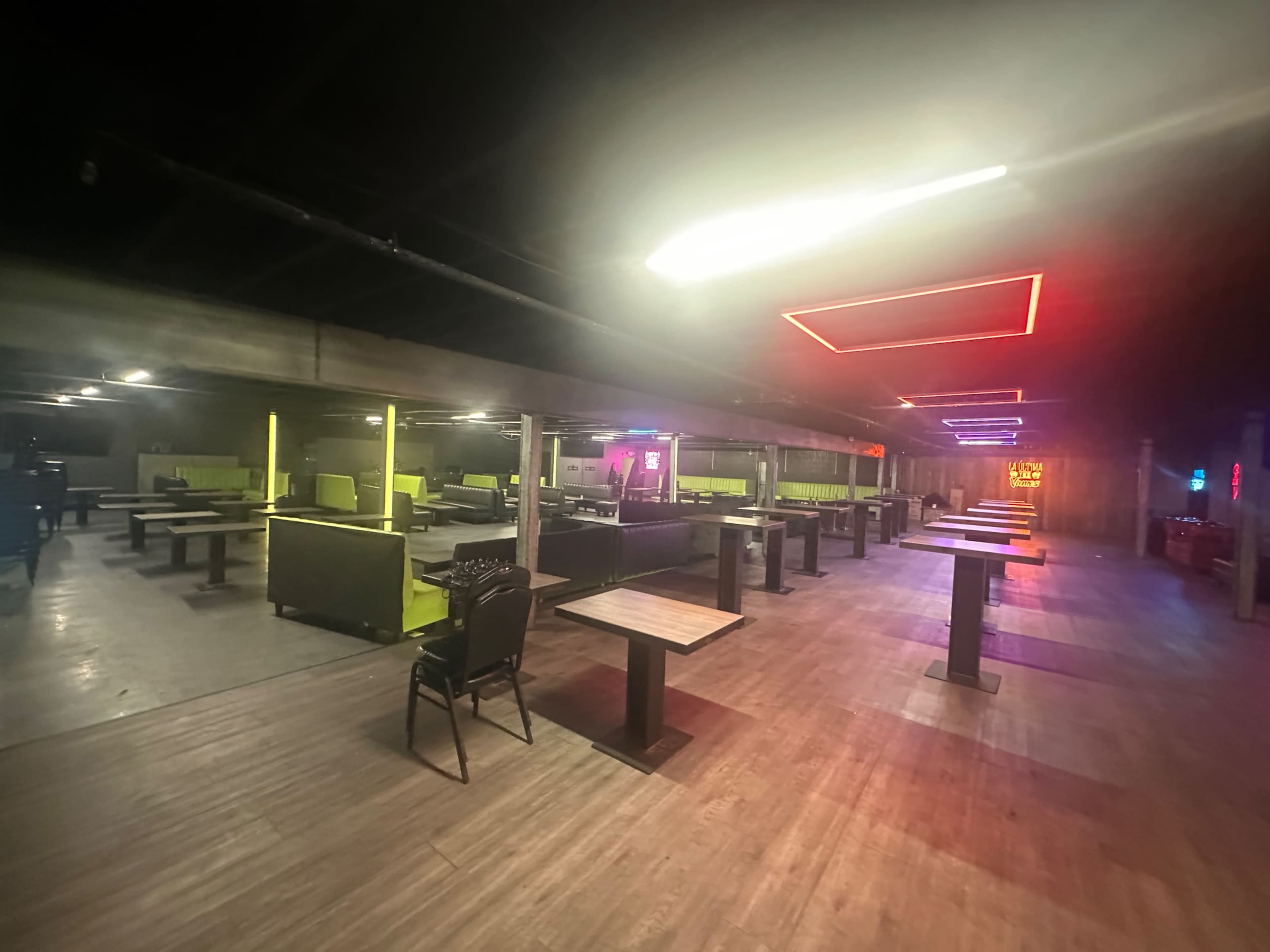 The image shows an indoor venue with multiple seating areas, featuring tables and chairs arranged under colorful neon lights.