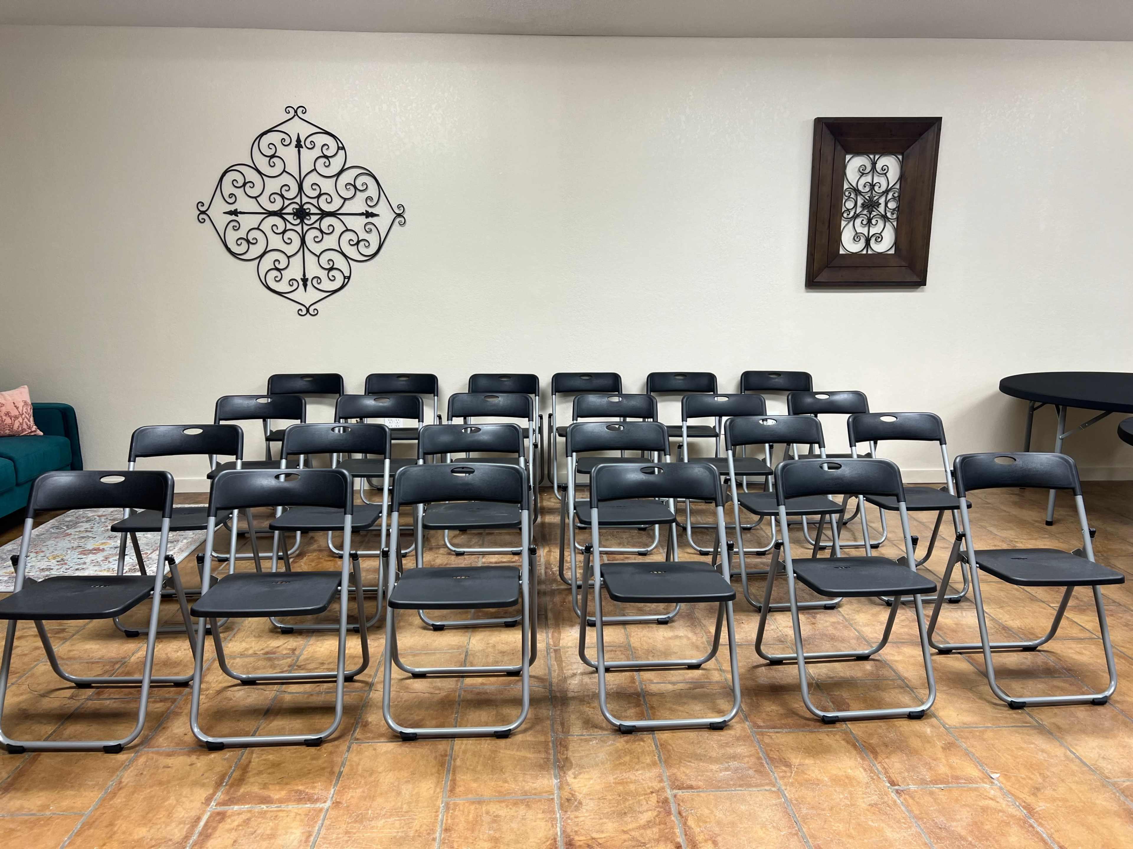 A room set up with rows of black folding chairs facing a wall with decorative elements.