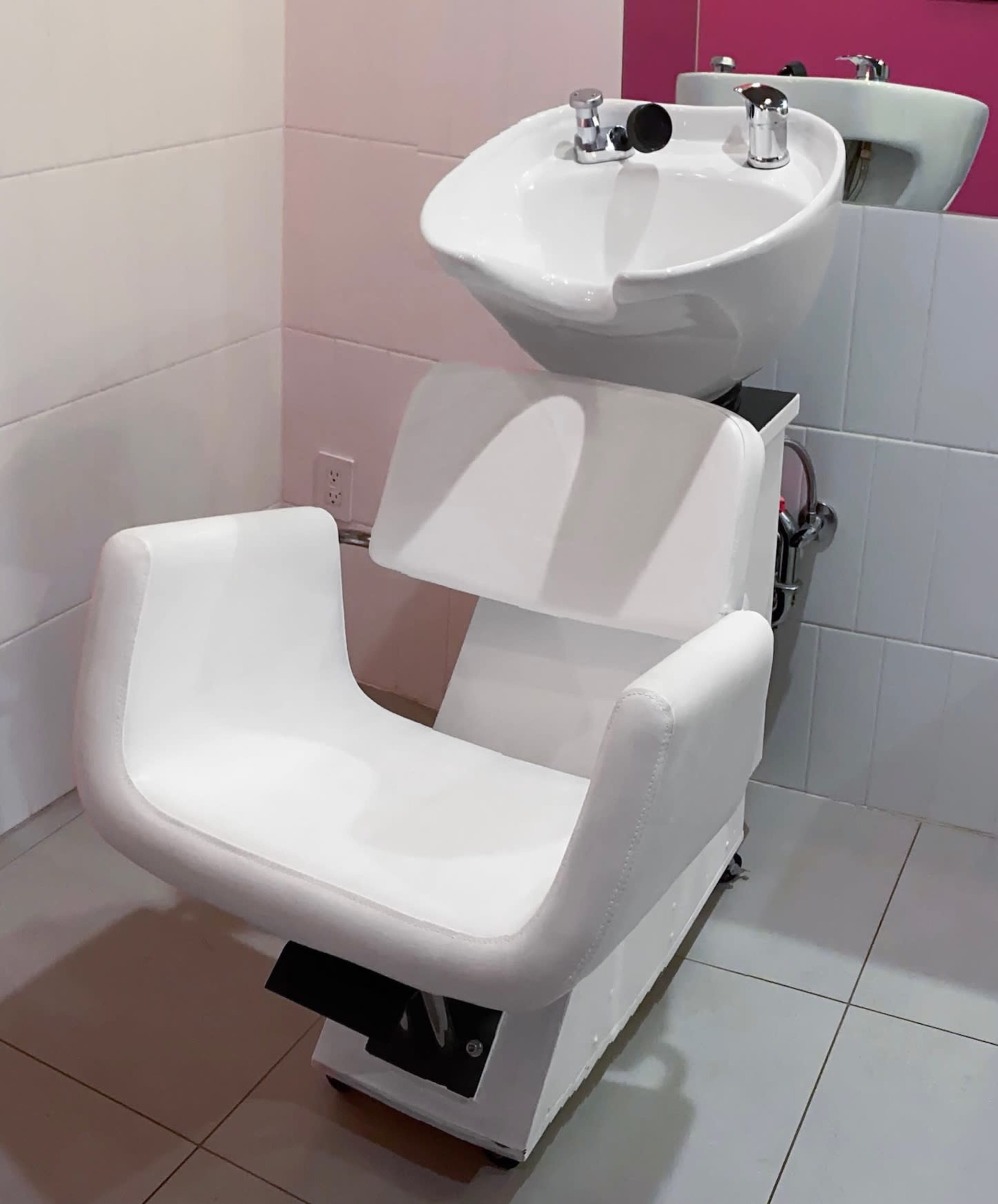 The image shows a hair washing station featuring a white chair positioned beneath a sink with a curved basin.