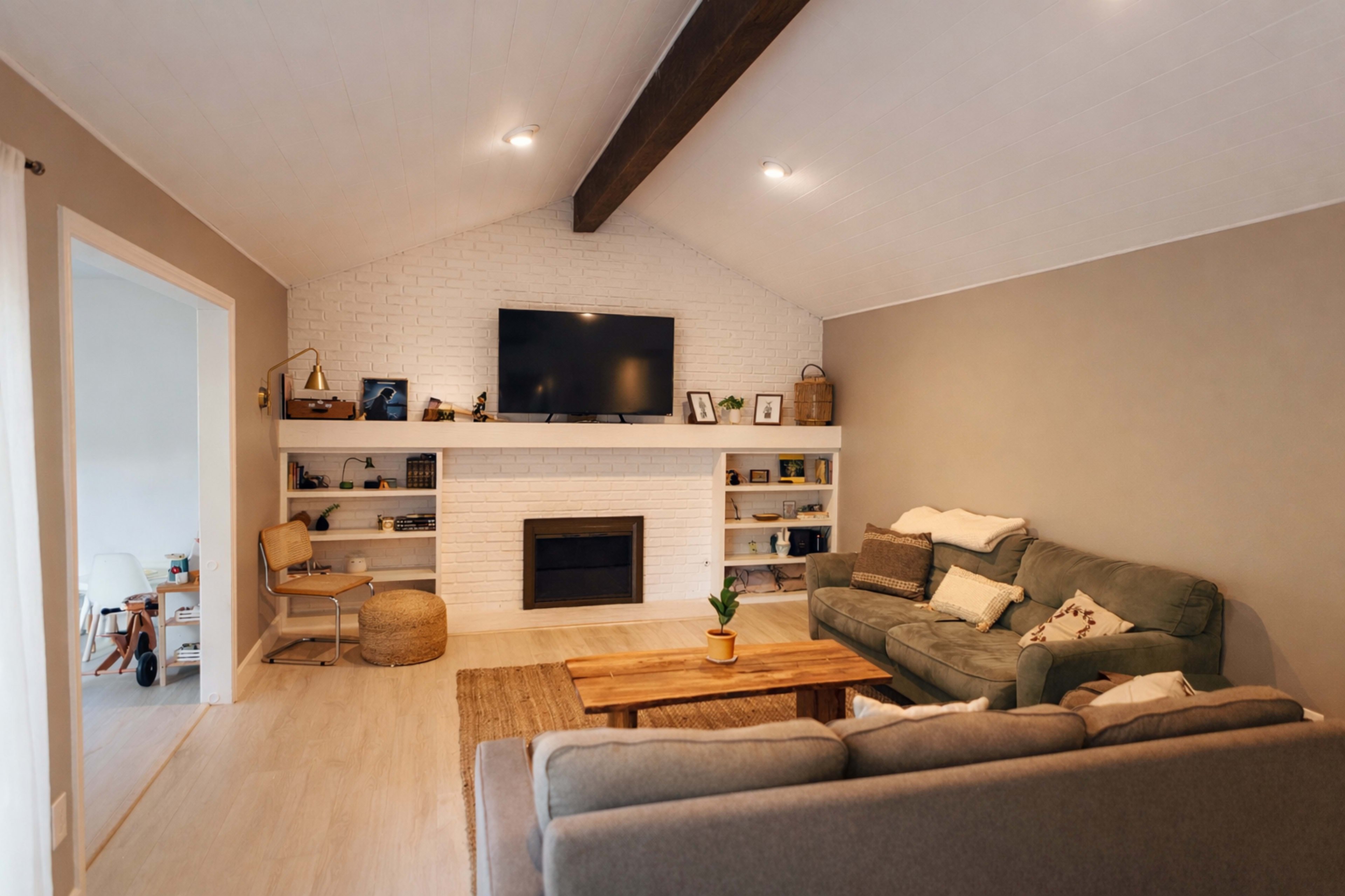 The living room features a comfortable seating area with two sofas facing a white-brick fireplace and a mounted television, surrounded by built-in shelves filled with decor and books.