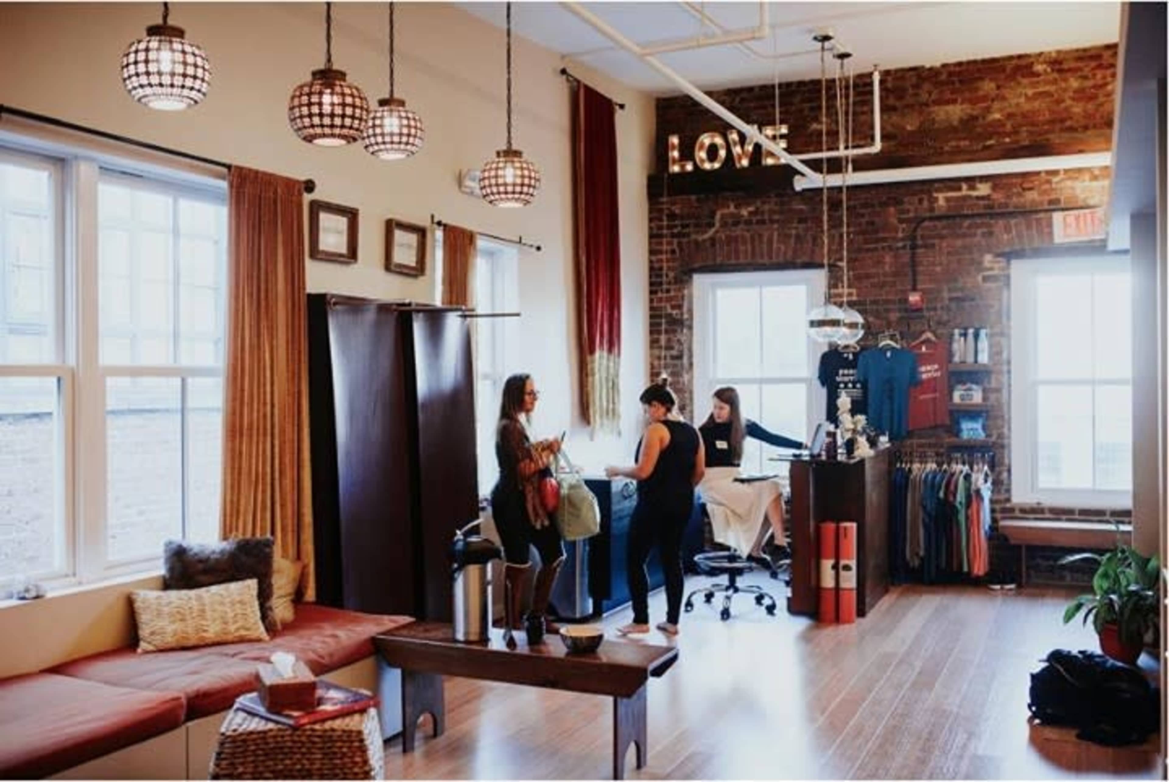 A stylish retail space features a sofa area, a clothing display, and two people engaged in a discussion near a workspace.