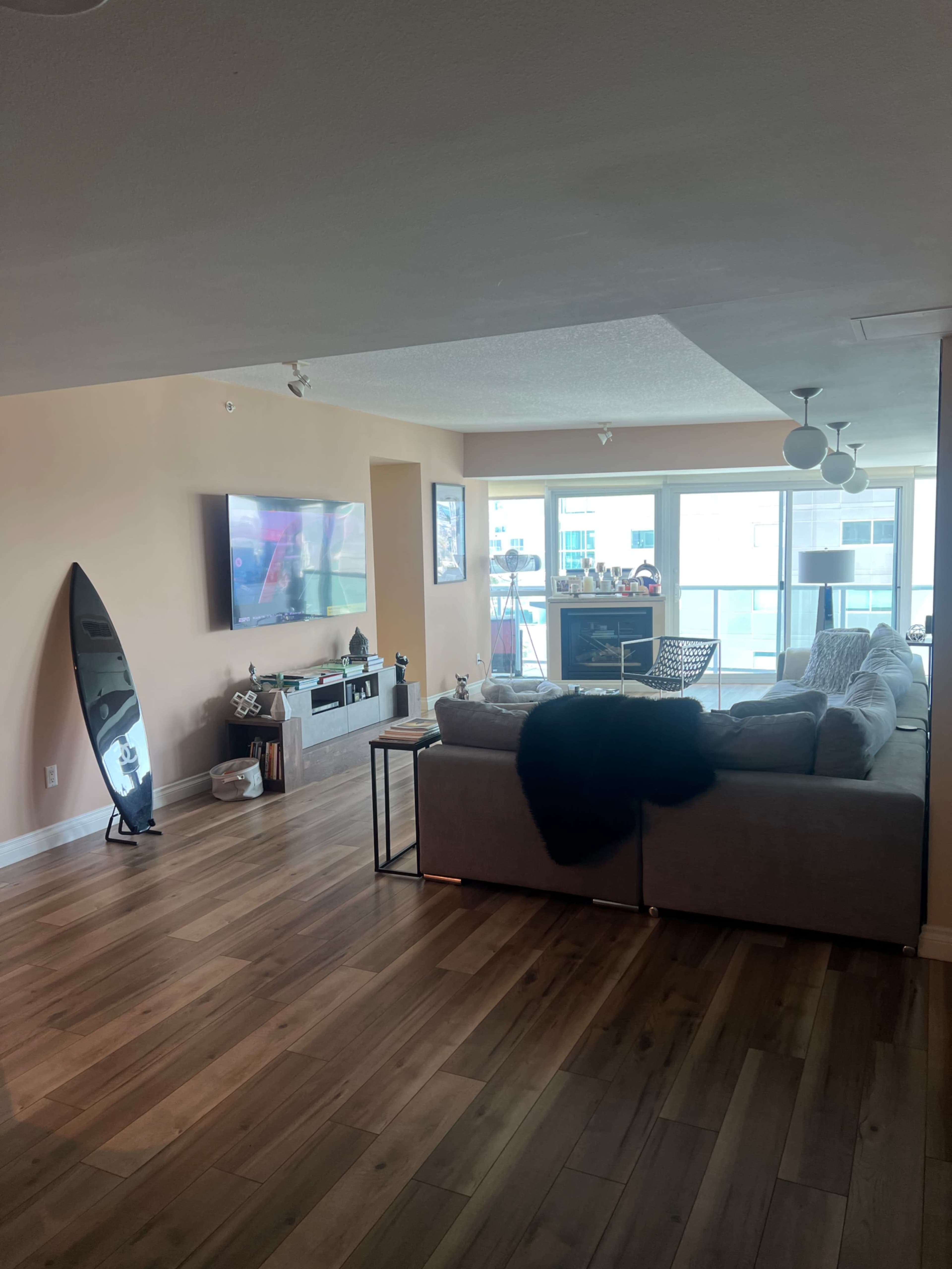 A modern living room with a large sofa, a television mounted on the wall, and a surfboard leaning against the wall.