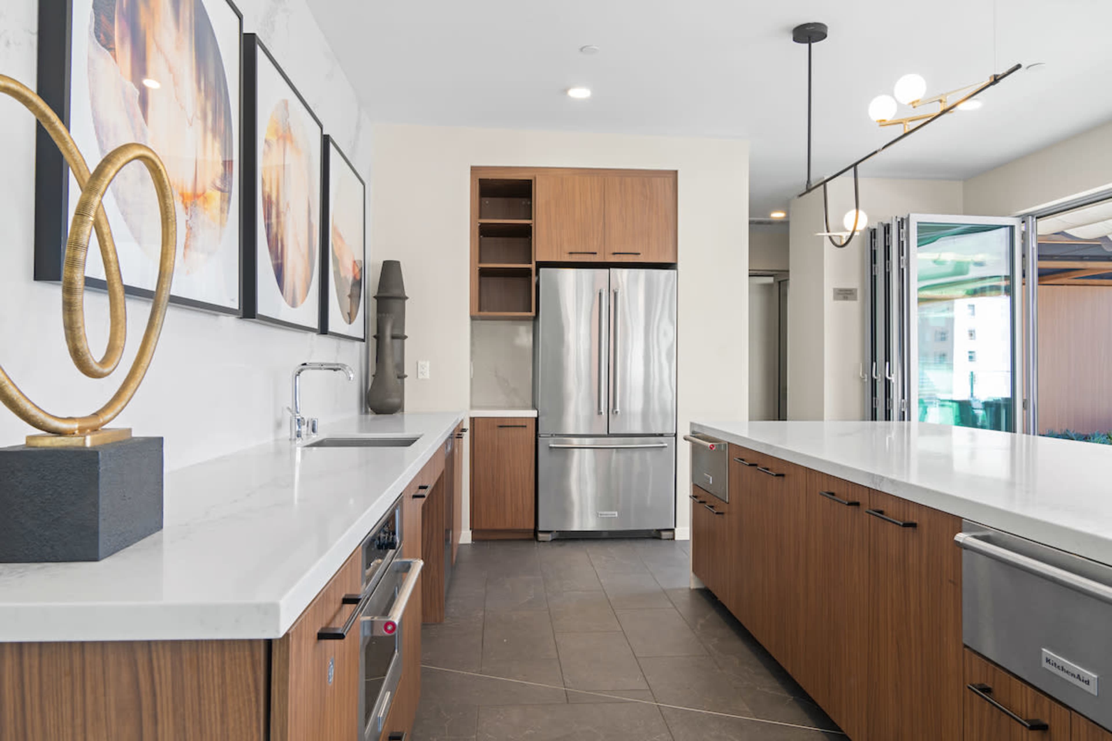The image shows a modern kitchen featuring wooden cabinets, a stainless steel refrigerator, and a marble countertop.