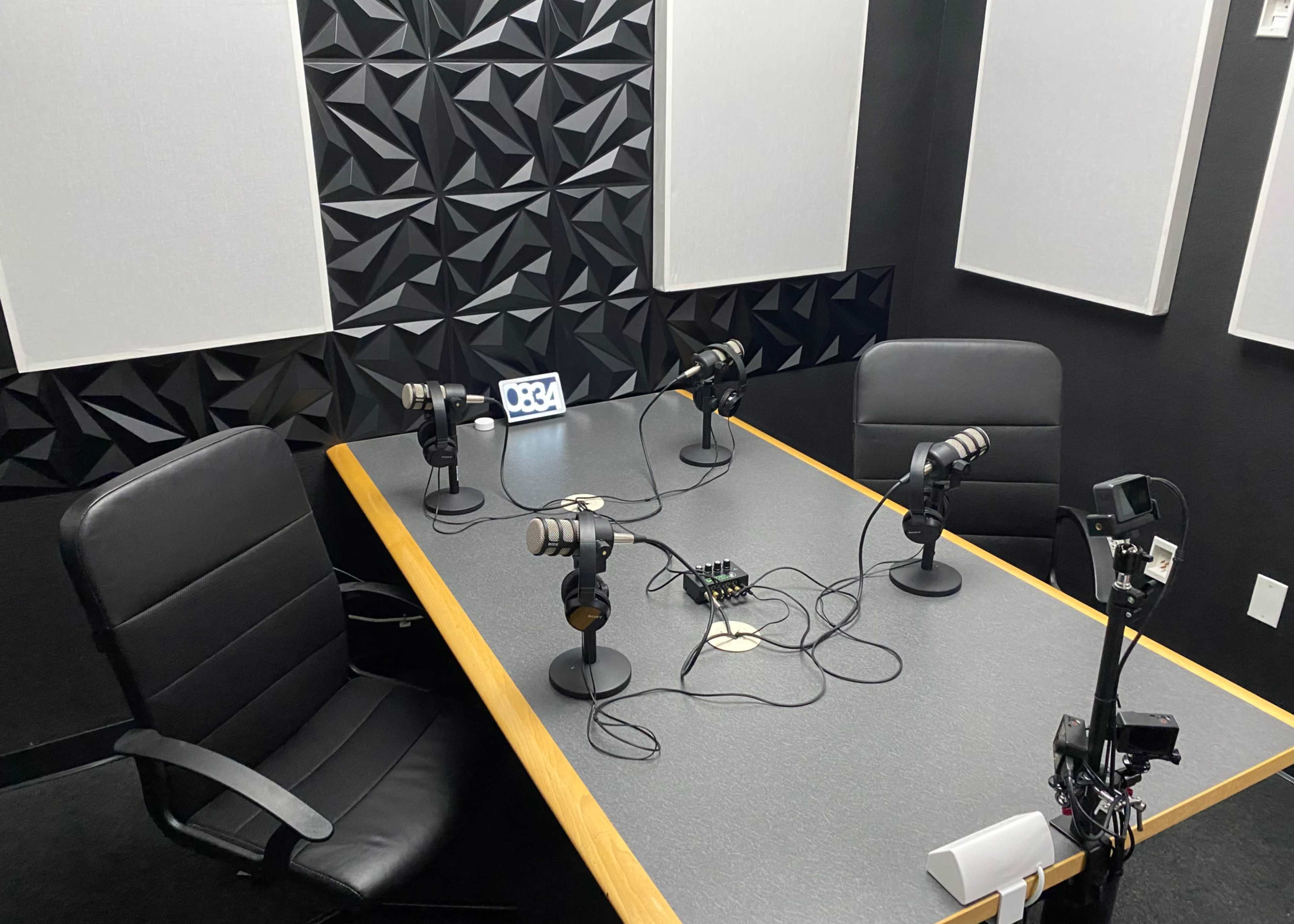 A quiet recording studio features a table with four microphones, two chairs, and soundproof wall panels.
