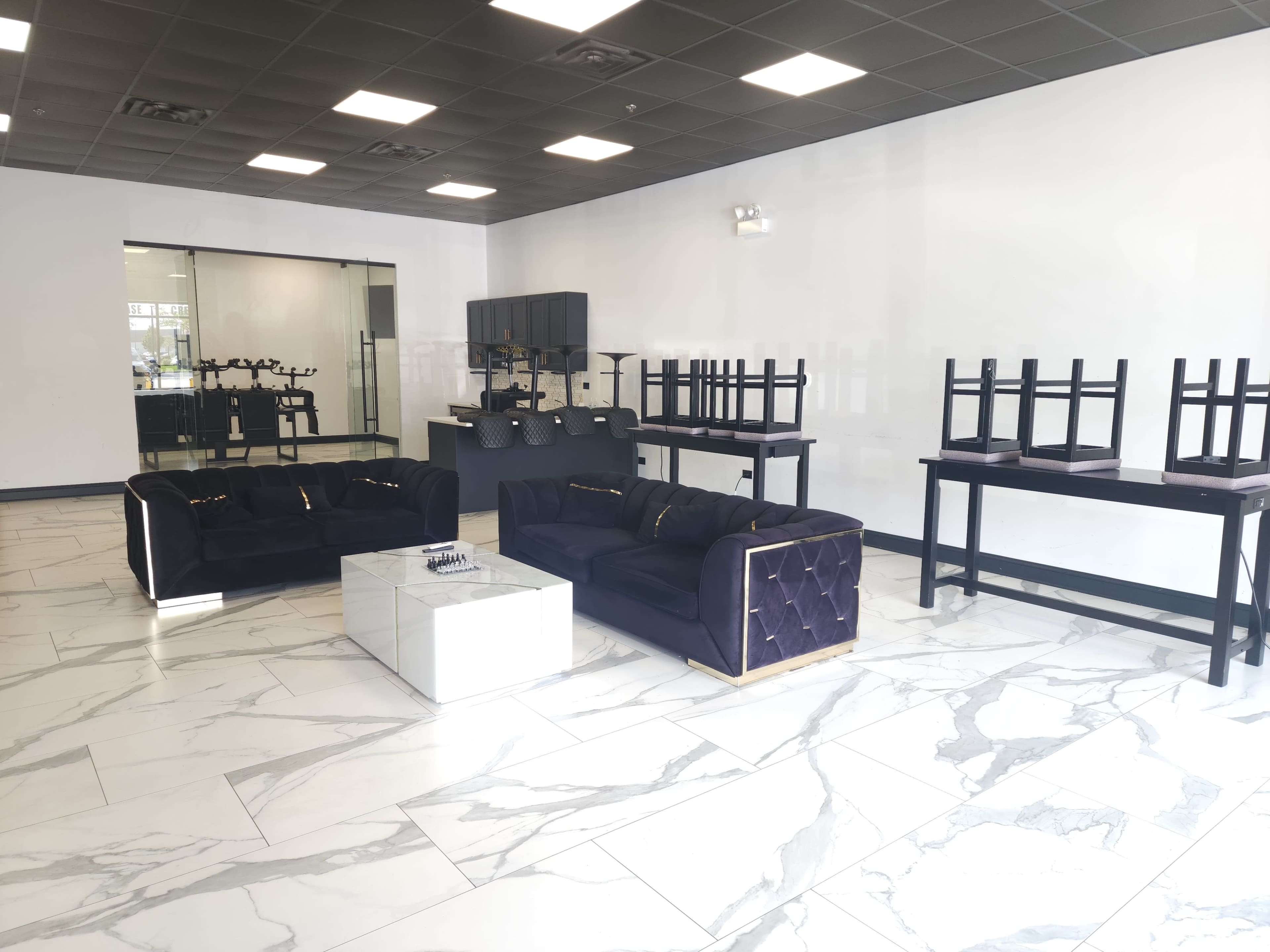 The image shows a modern, empty showroom with dark velvet sofas, a glass-topped table, and several tables turned upside down against the walls.