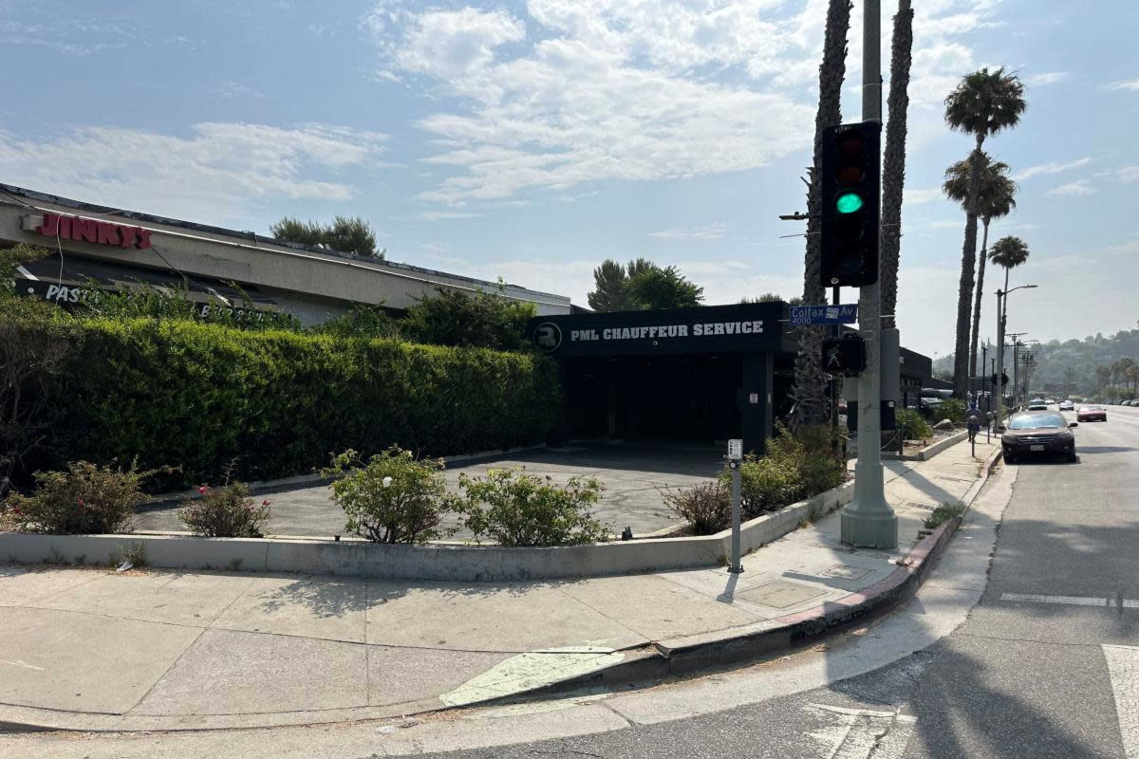 The image shows a vacant chauffeur service building surrounded by greenery at a street corner, with palm trees lining the road.