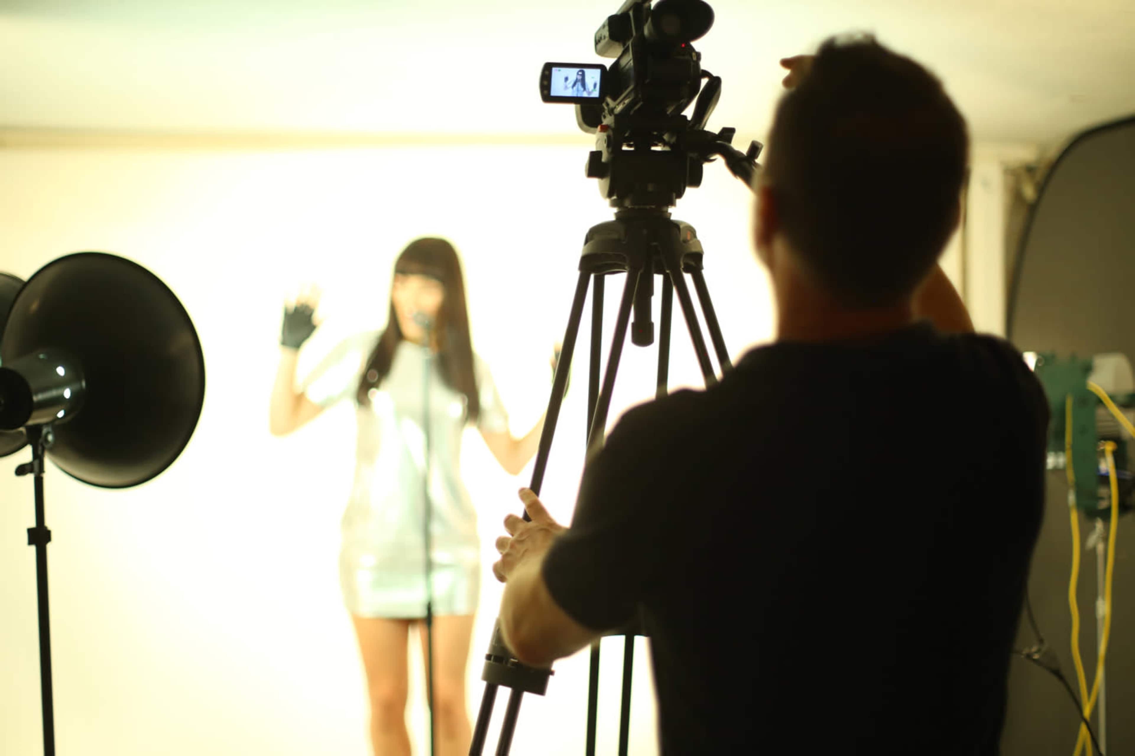 A camera operator adjusts equipment while a model poses against a lit backdrop.
