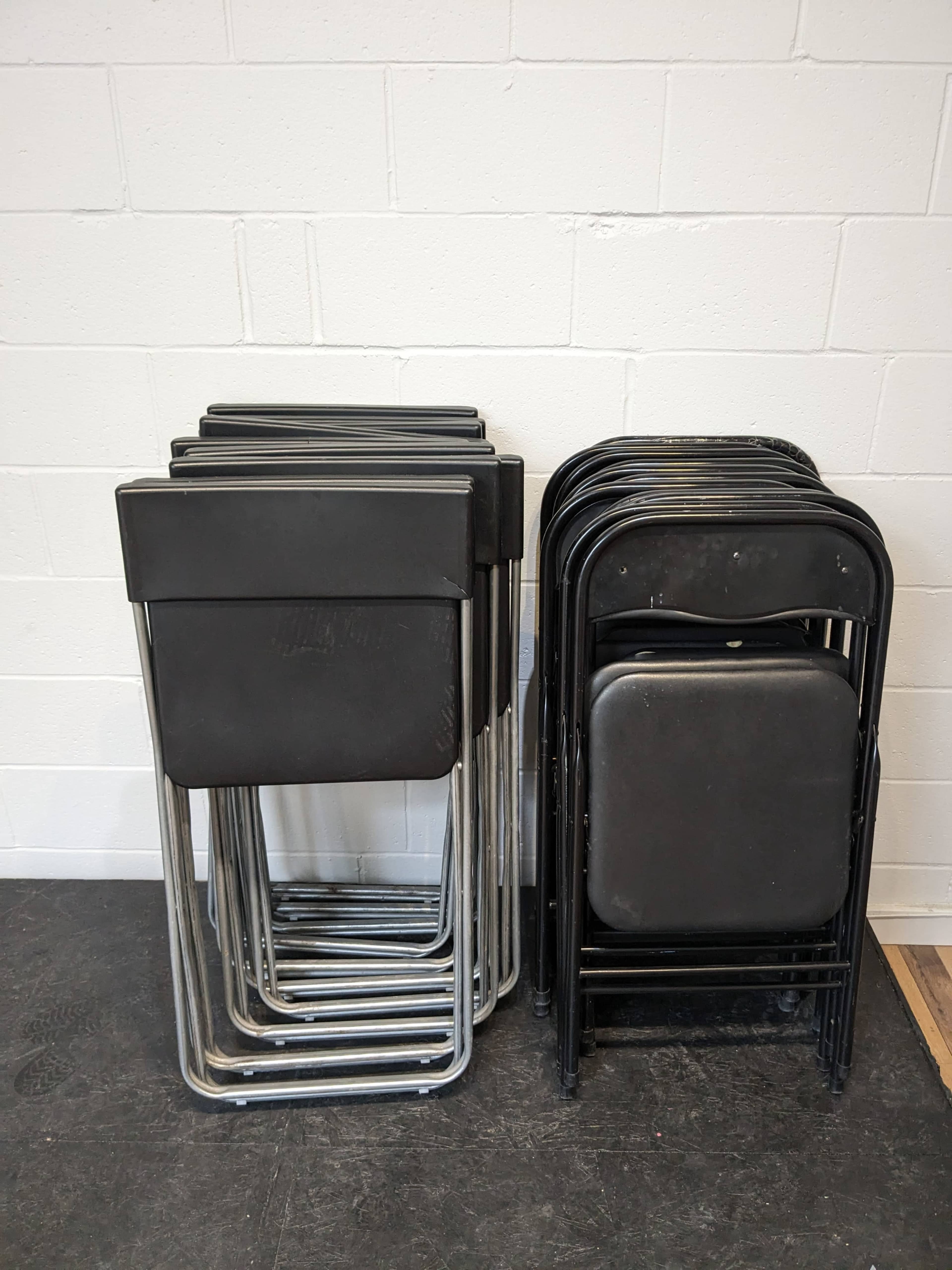 A stack of black folding chairs is arranged neatly against a white wall.