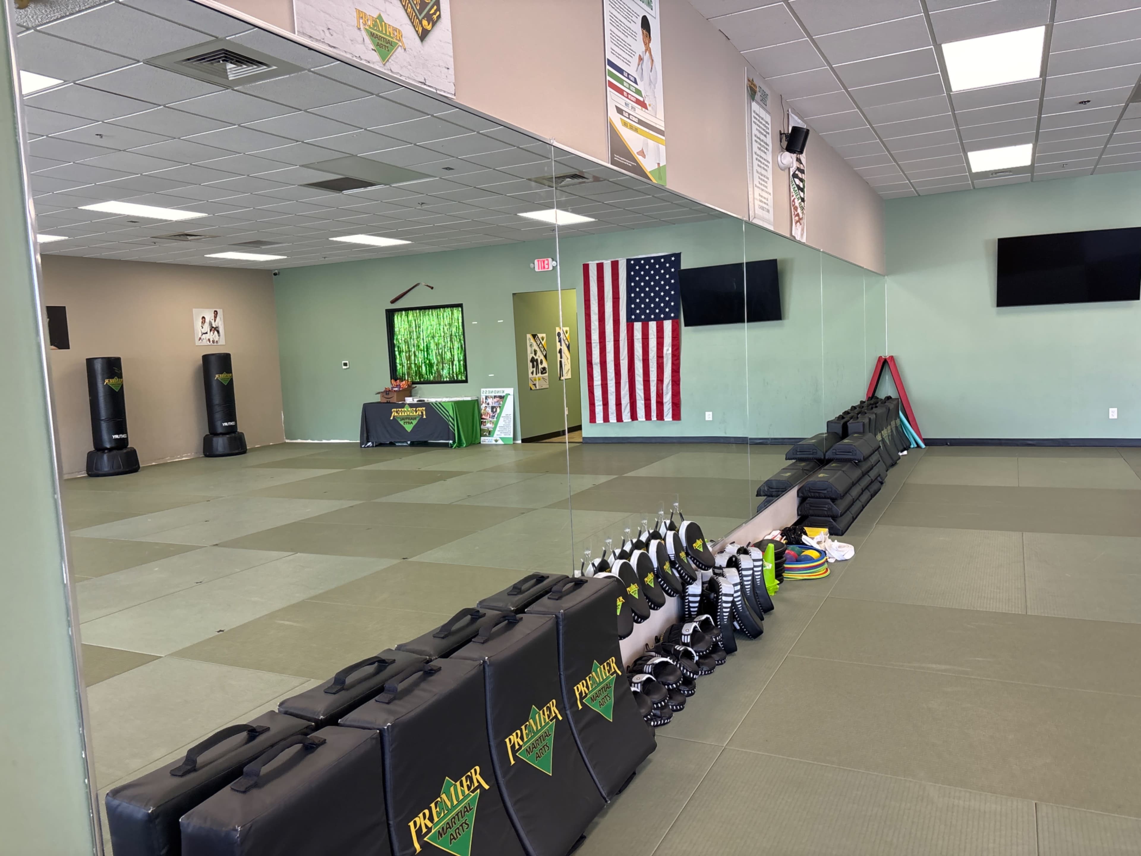 The image shows an empty martial arts studio with mirrors, padded flooring, and training equipment neatly arranged along one side.