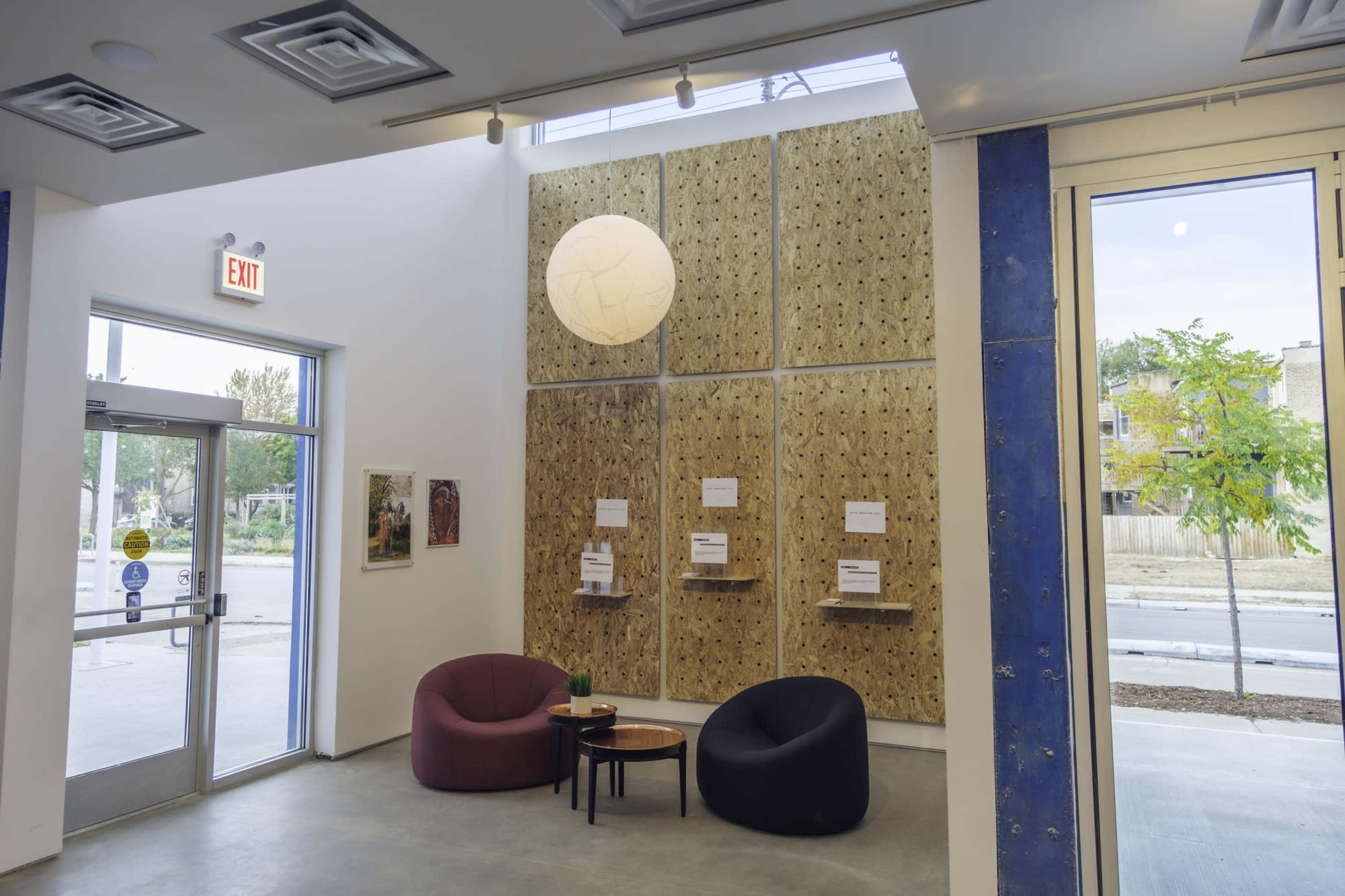 The image shows a modern interior space with two armchairs, a small coffee table, and a textured wooden wall, illuminated by a large pendant light.