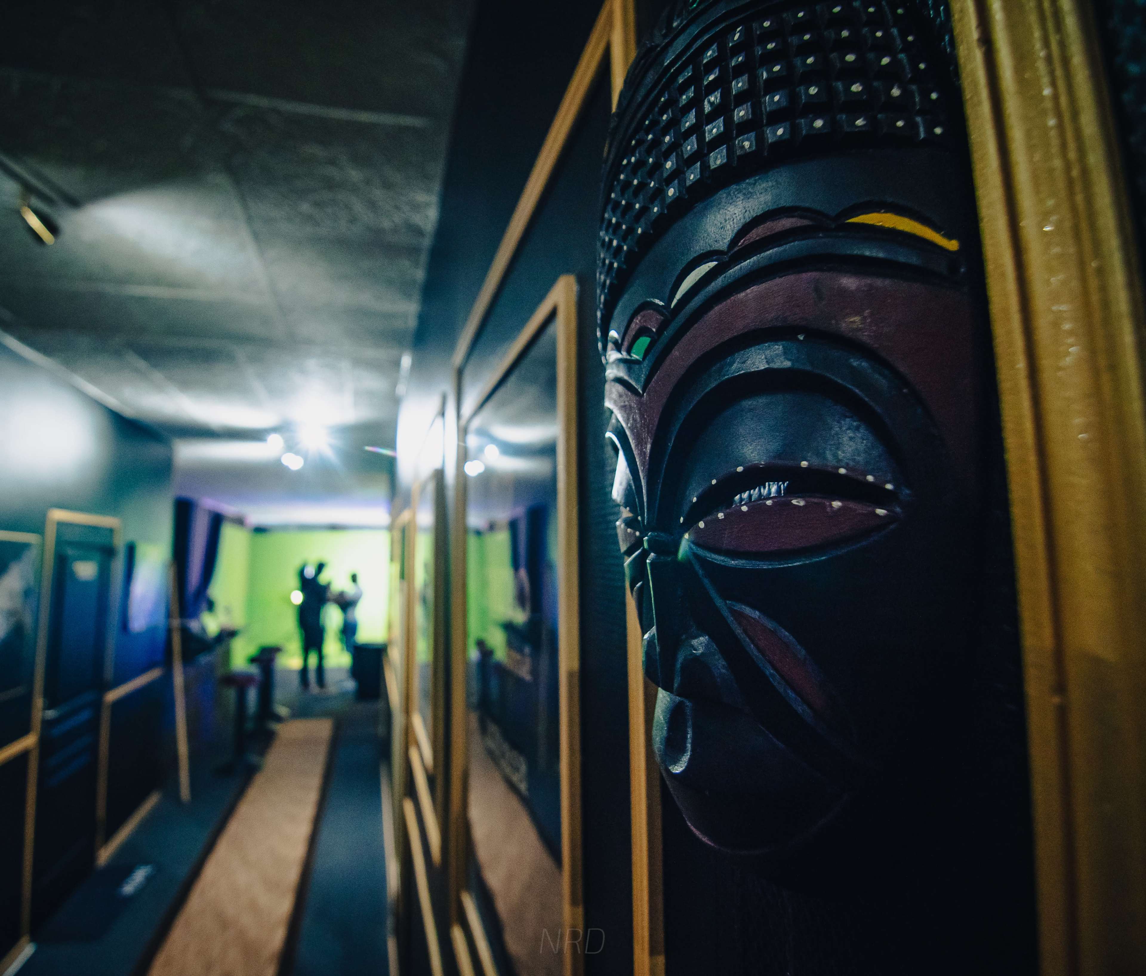 A carved mask adorns the wall of a dimly lit hallway leading to a brightly lit green room.