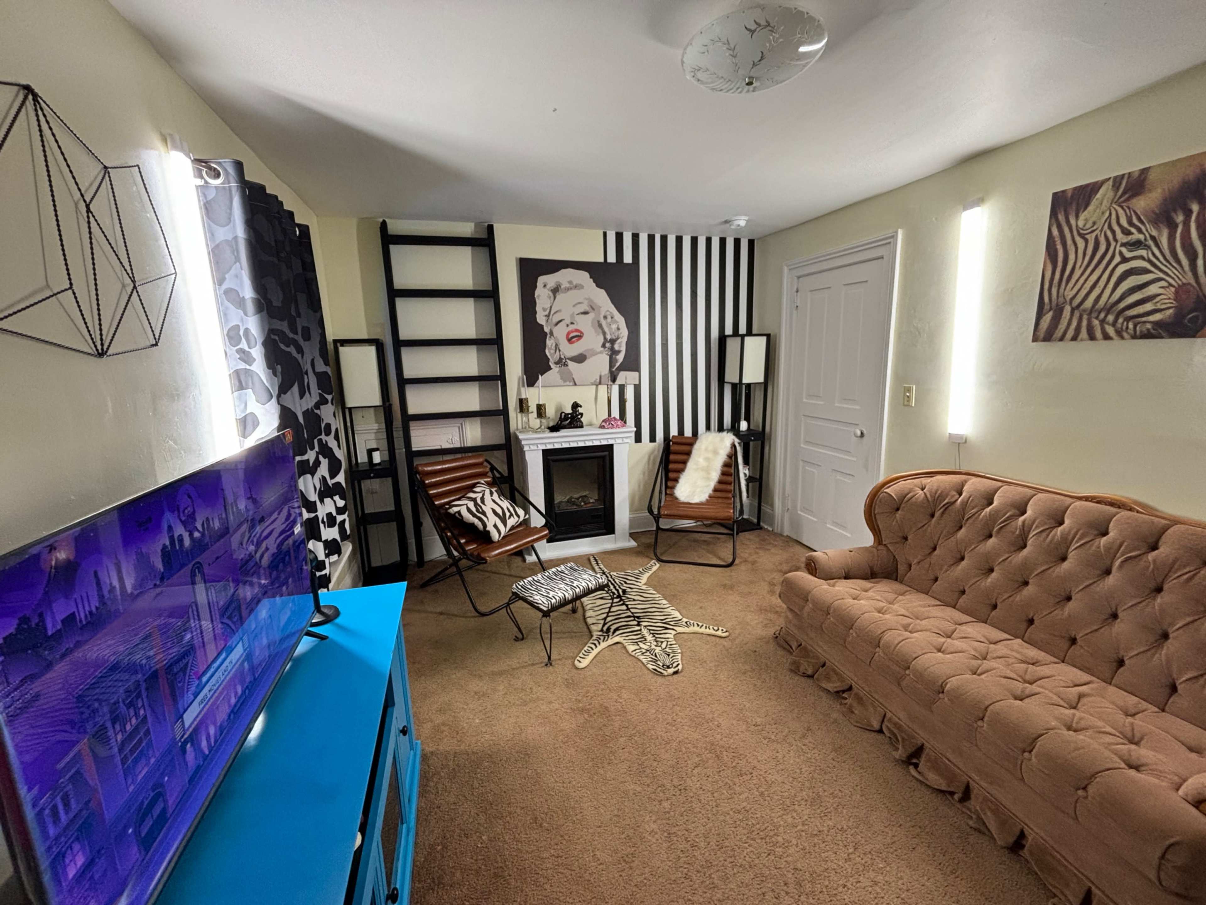 The image shows a living room with a brown couch, a television on a blue stand, a small fireplace, and walls featuring black and white decor.
