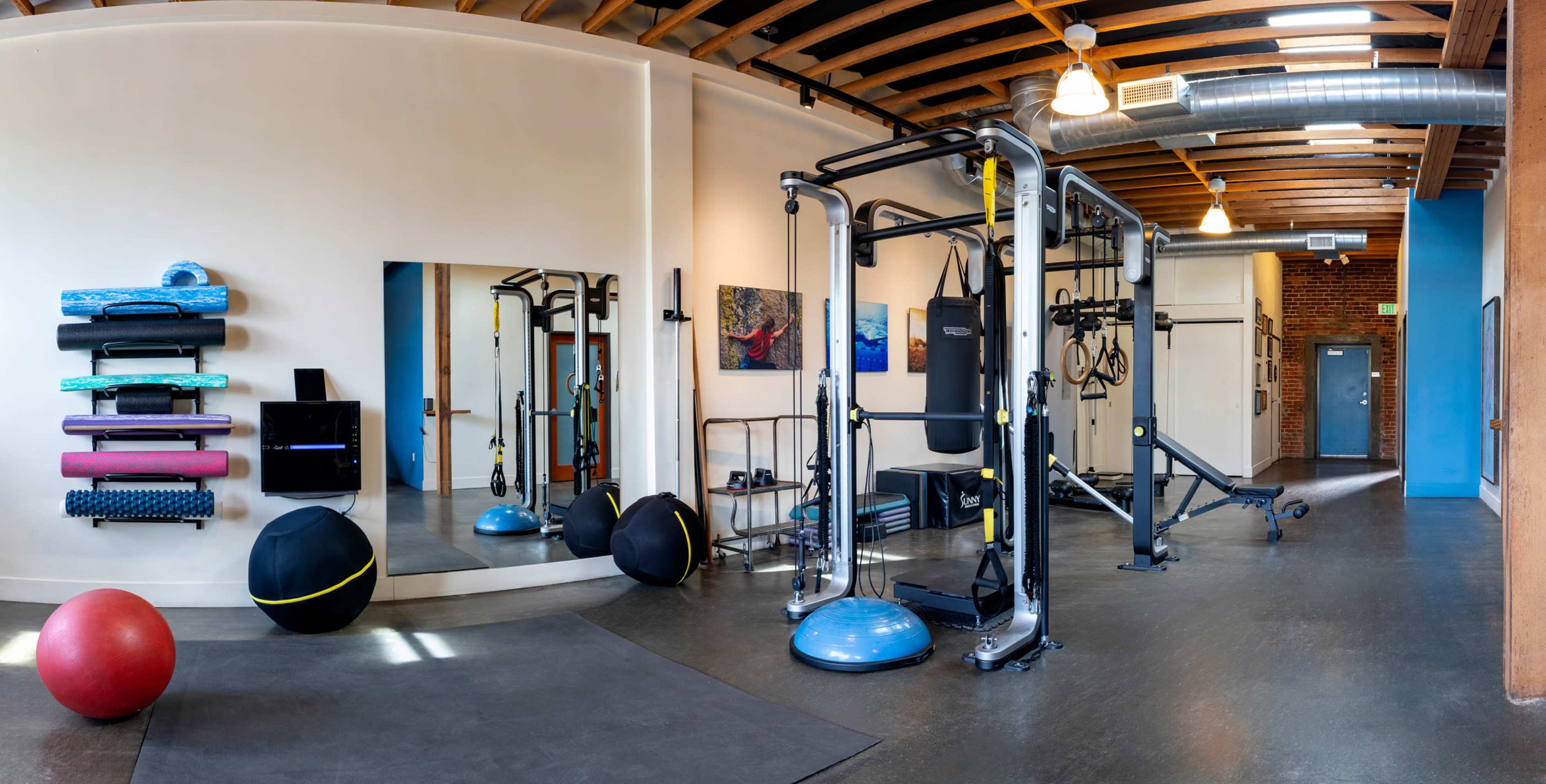 A fitness studio equipped with exercise machines, balance balls, mats, and wall-mounted artwork.