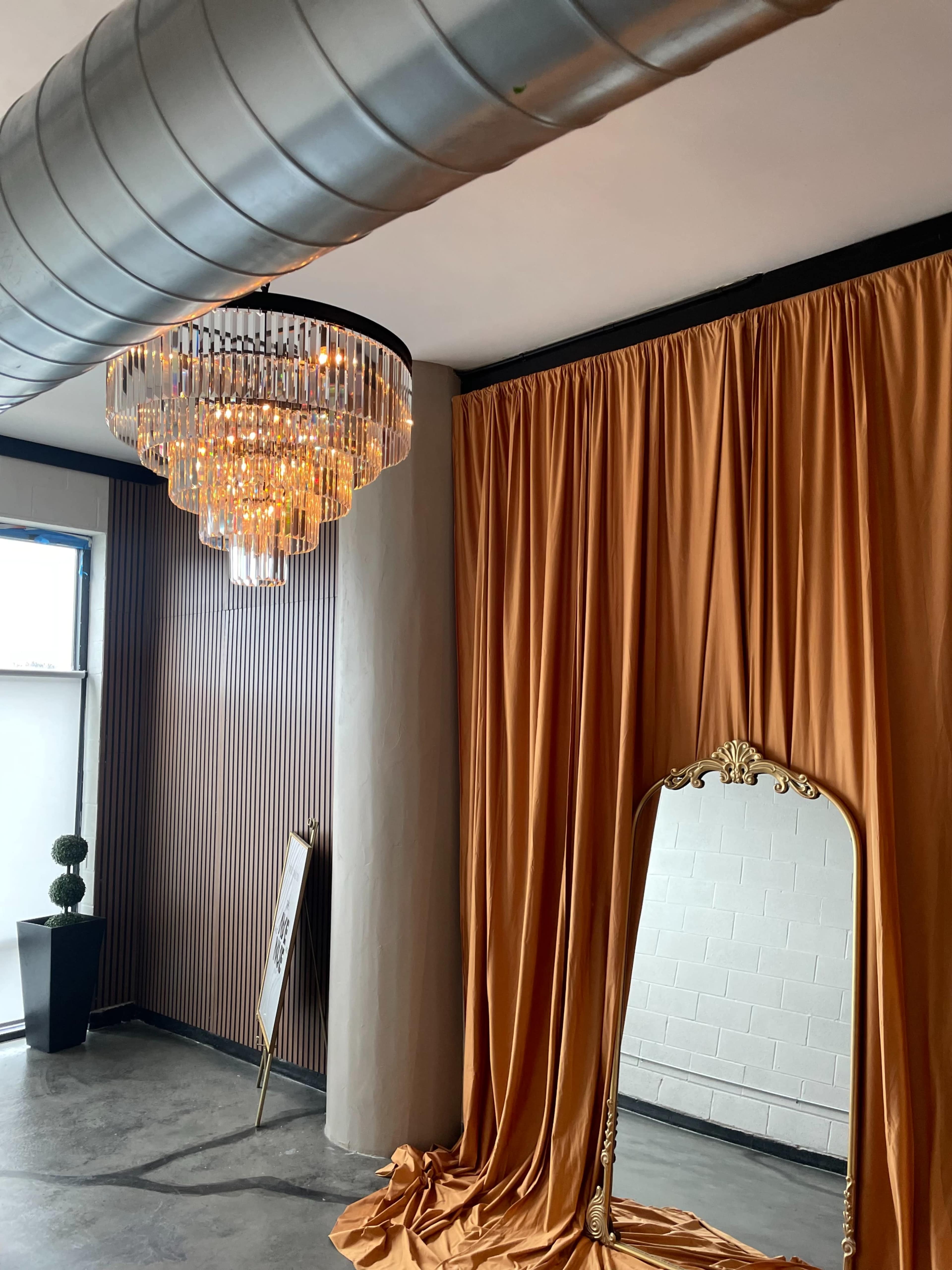 The image features a room with an elegant chandelier, an ornate mirror, and draped orange fabric against a textured wall.