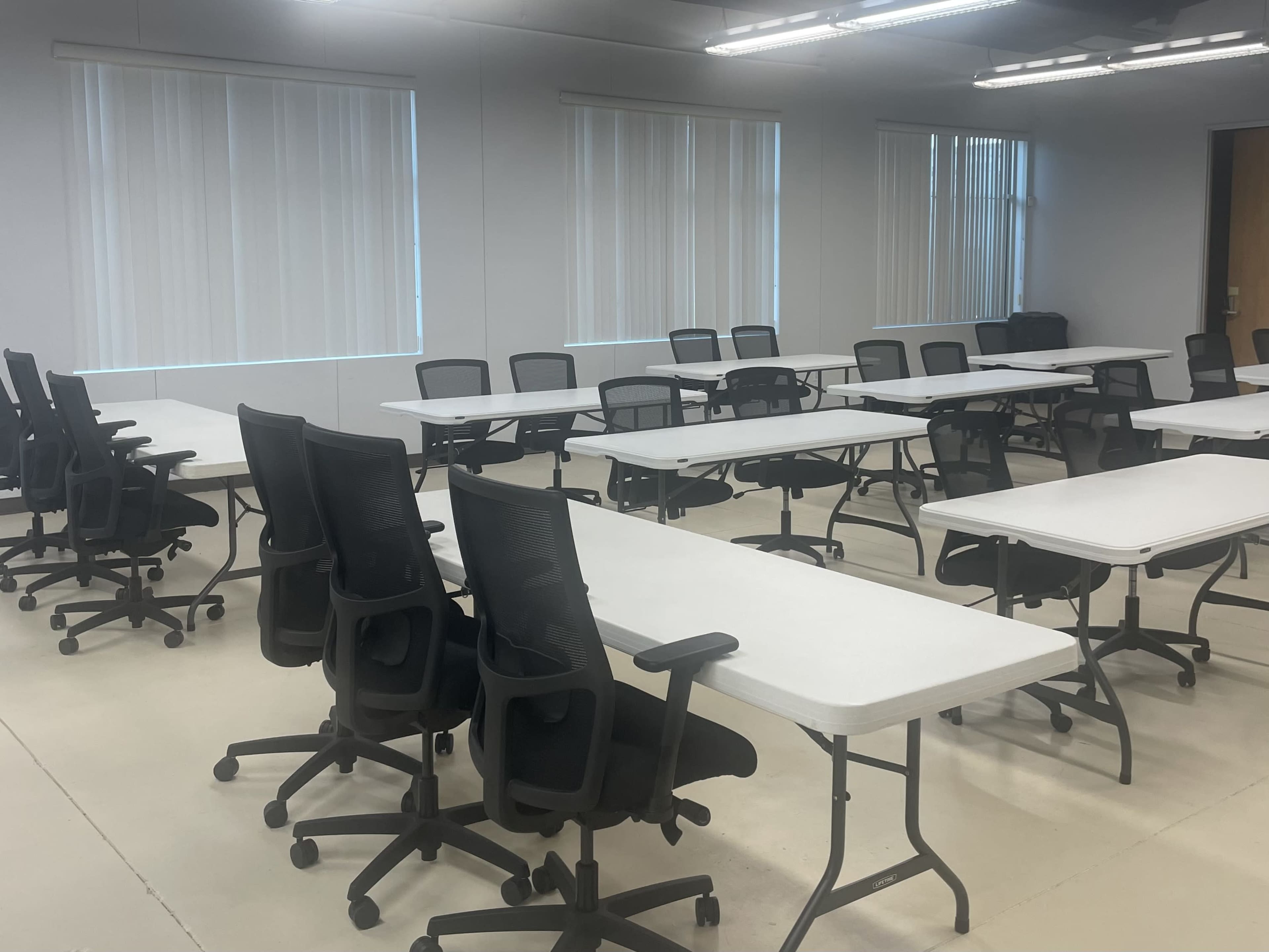 A large, empty meeting room features multiple rows of folding tables and chairs arranged in a grid pattern.