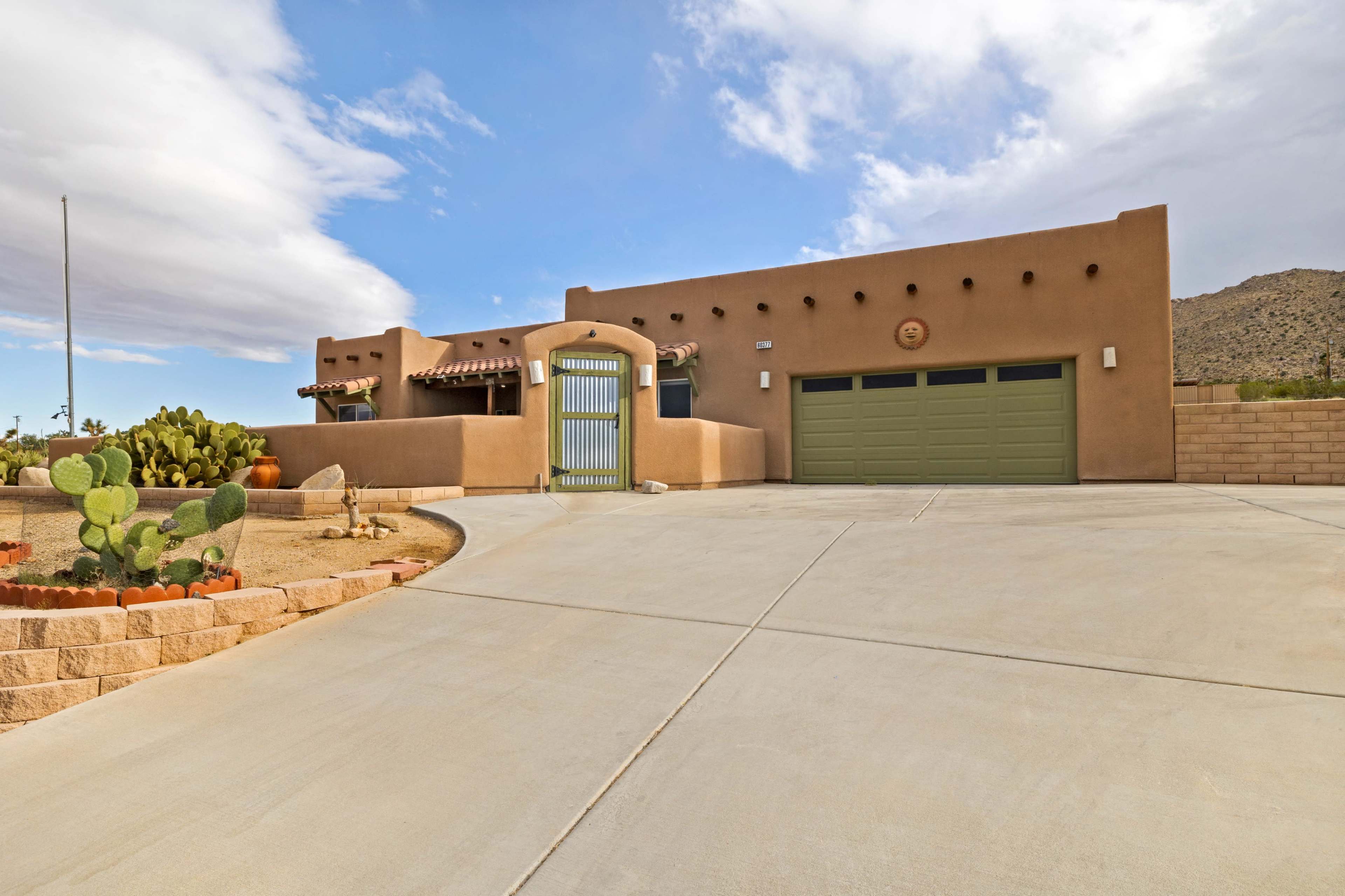The image shows a southwestern-style house with adobe architecture, a green garage door, and a desert landscape featuring cacti.