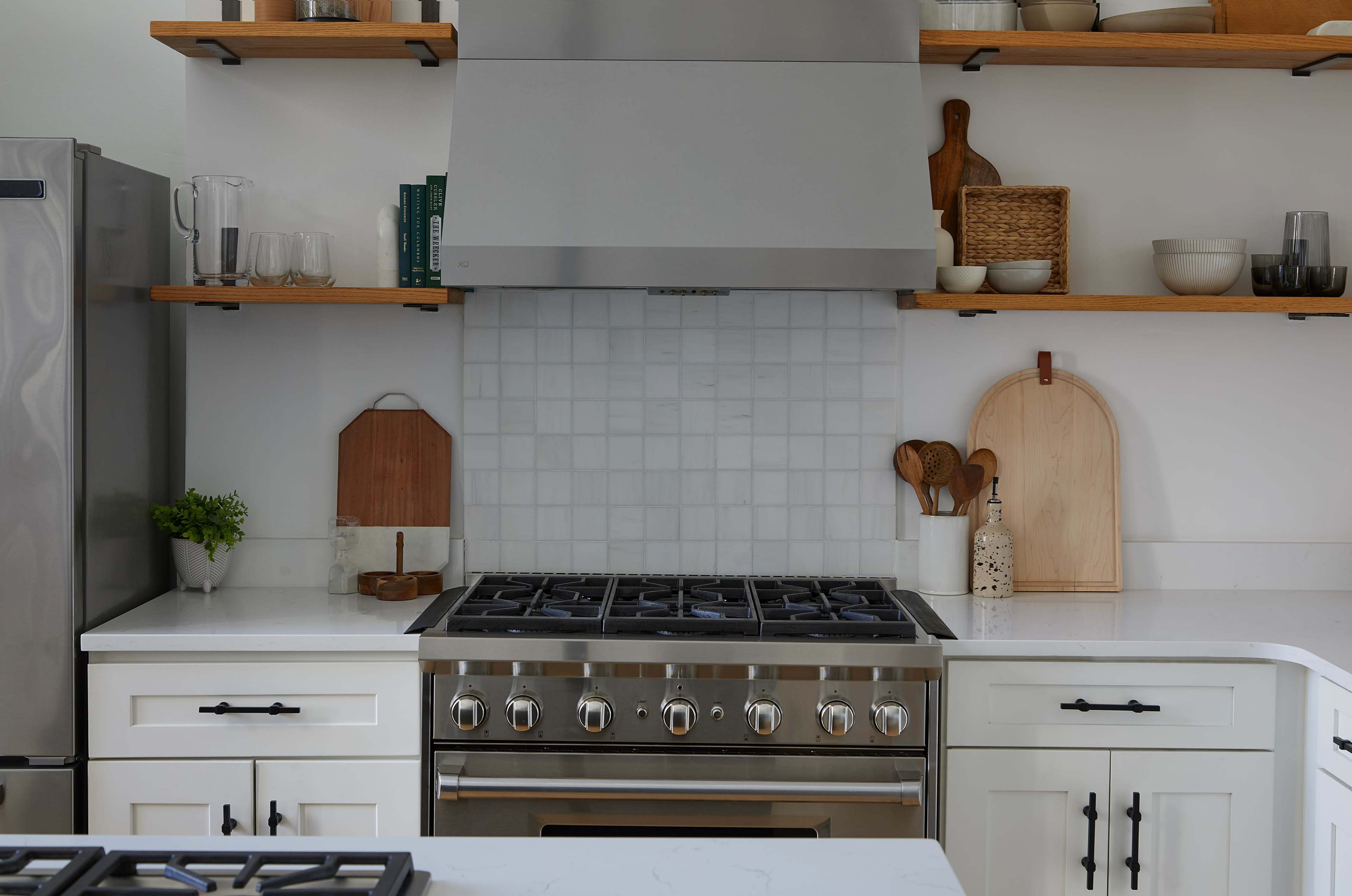 A modern kitchen features stainless steel appliances, a large gas range, and open shelving with wooden accents.