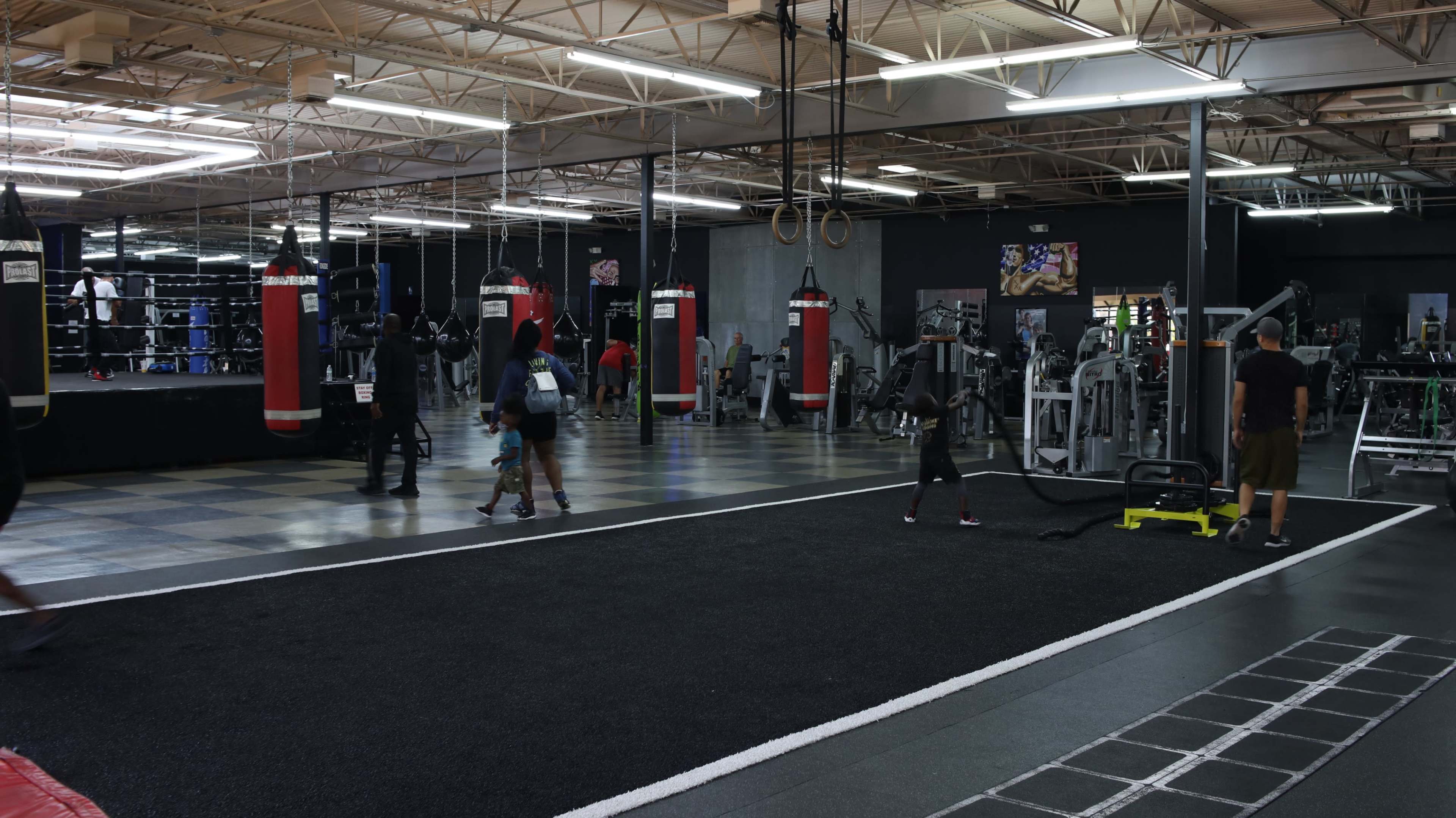 A fitness gym features several punching bags, exercise equipment, and people engaged in various workouts.