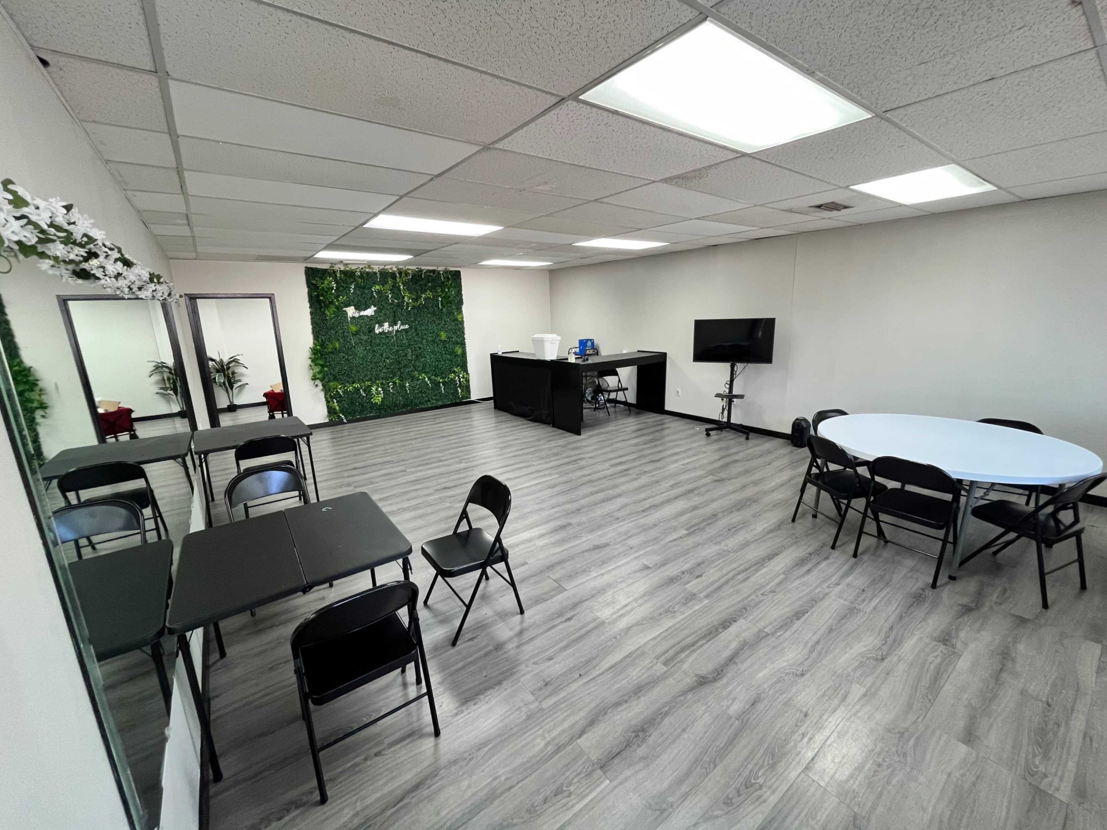 A spacious room features a green accent wall, multiple tables and chairs, and a large mirror on one side.
