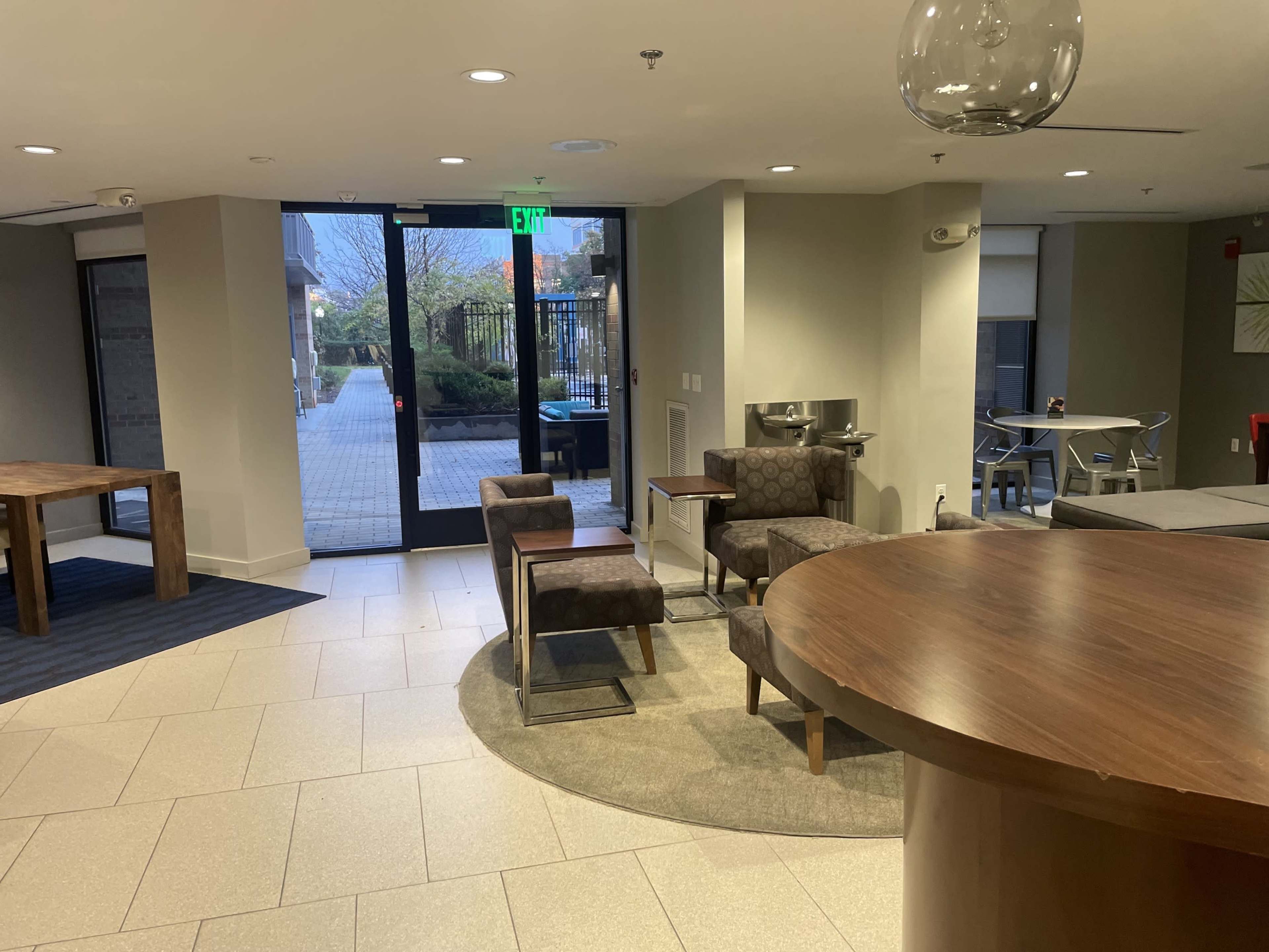 A modern lobby with a seating area, a round wooden table, and large glass doors leading to an outdoor space.