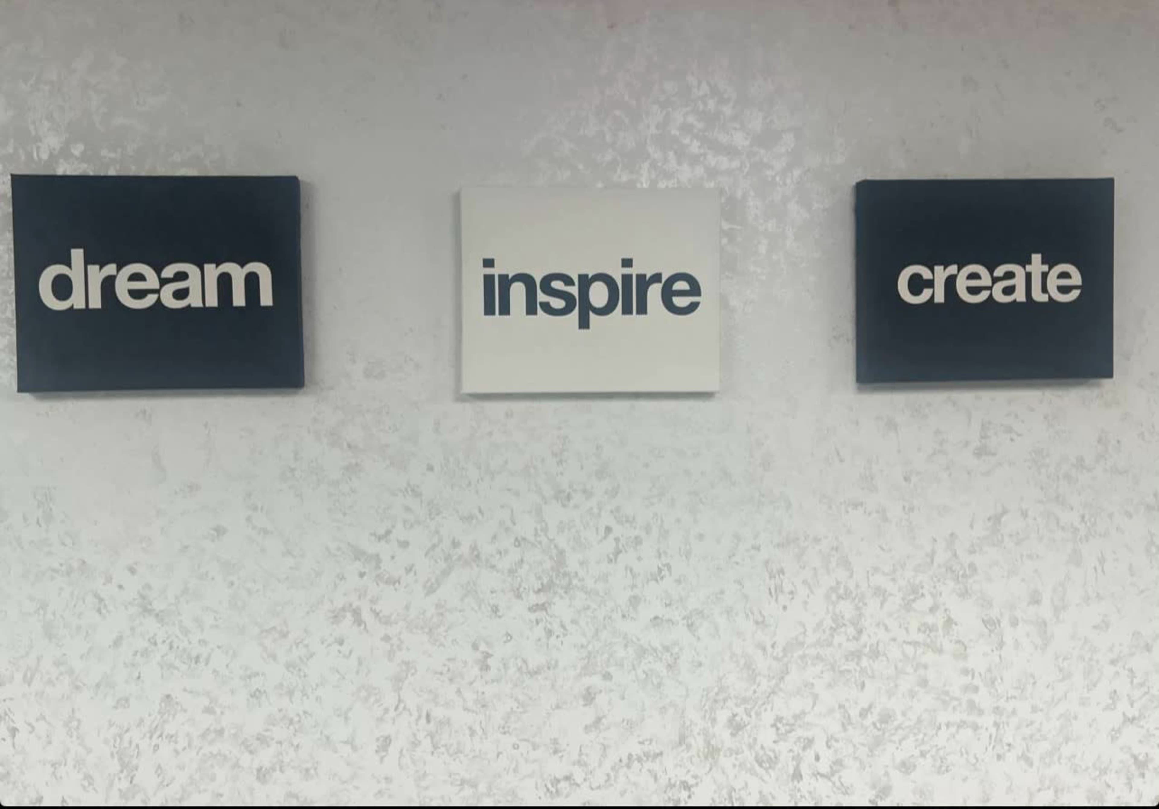 The image shows three wall-mounted canvases displaying the words "dream," "inspire," and "create" in white font against a blue background.