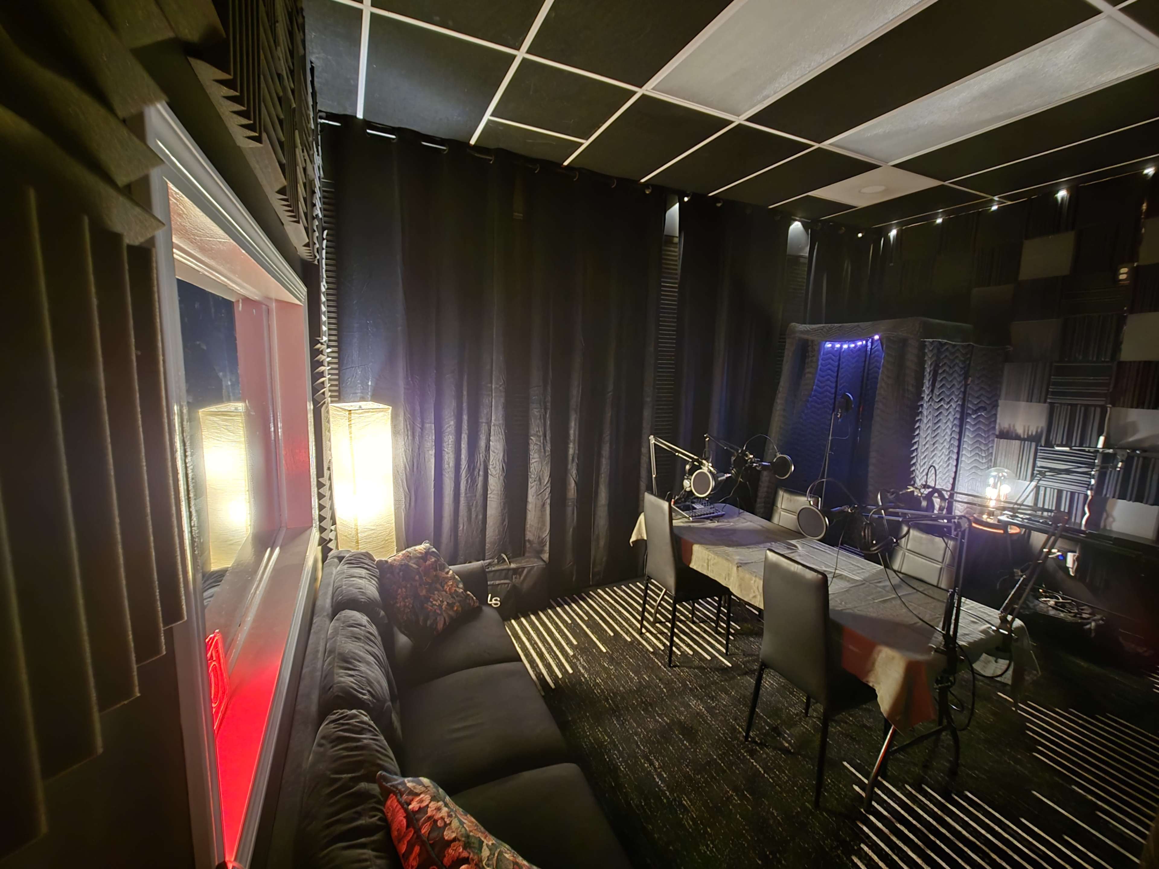 The image shows a soundproof recording studio featuring a dark interior with a couch, a table, and microphones set up in a corner.