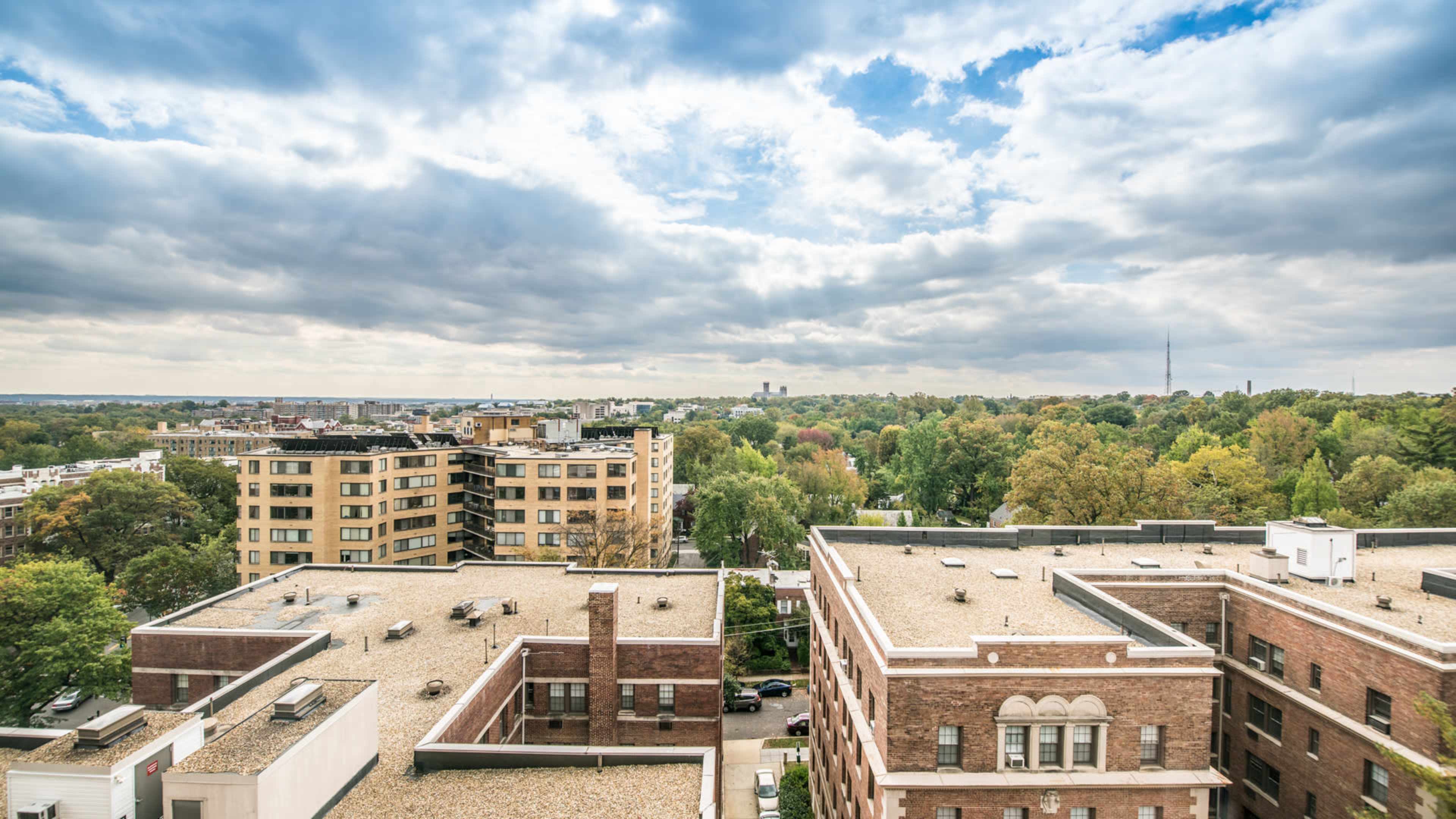 A view of urban apartments and green trees under a cloudy sky.
