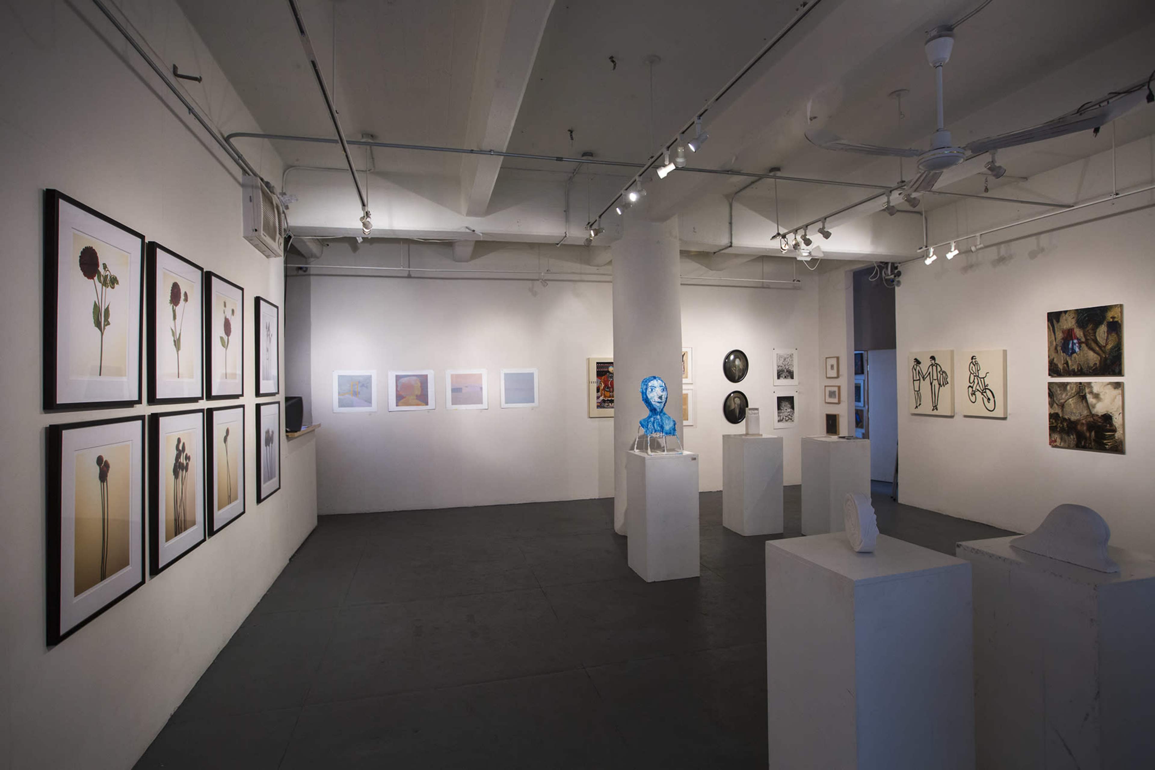The image shows an art gallery with various framed artworks displayed on the walls and sculptures on pedestals.
