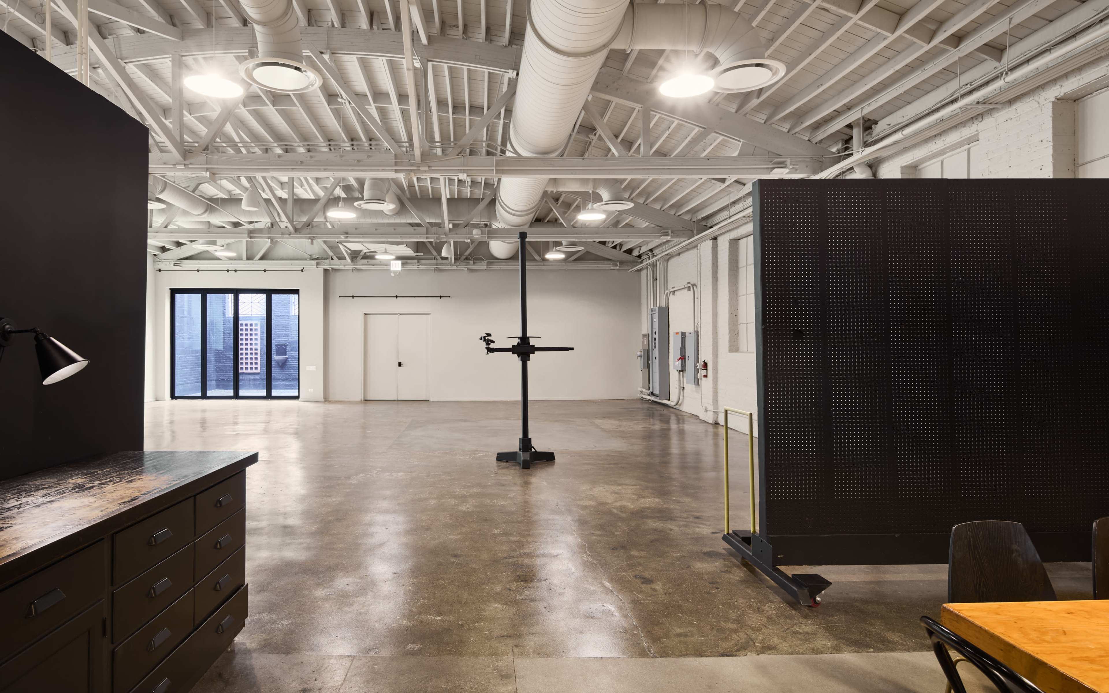 The image shows a spacious and modern interior with high ceilings, polished concrete flooring, and large windows illuminated by overhead lighting.