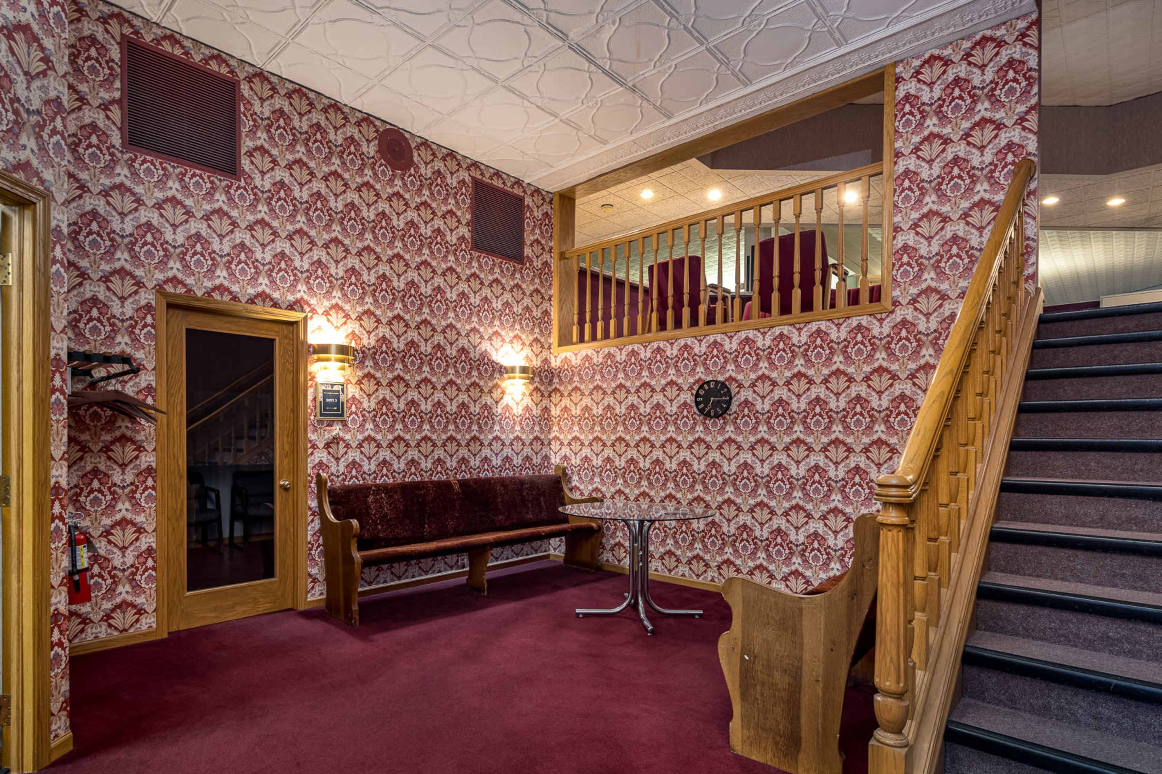 A staircase leading to an upper level in a room with patterned wallpaper, a wooden bench, and a round table.