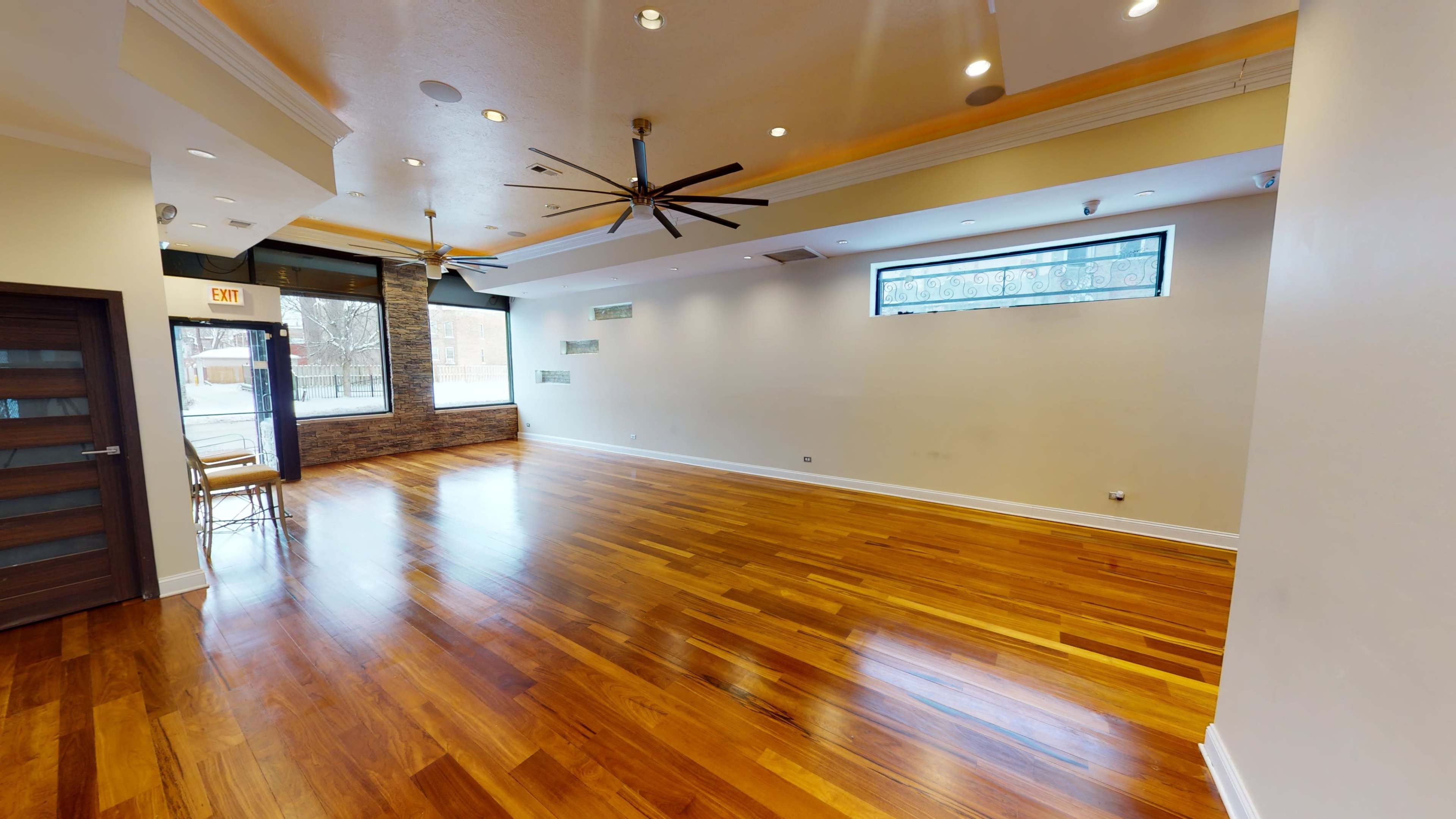 A spacious room with hardwood flooring, large windows, and ceiling fans.