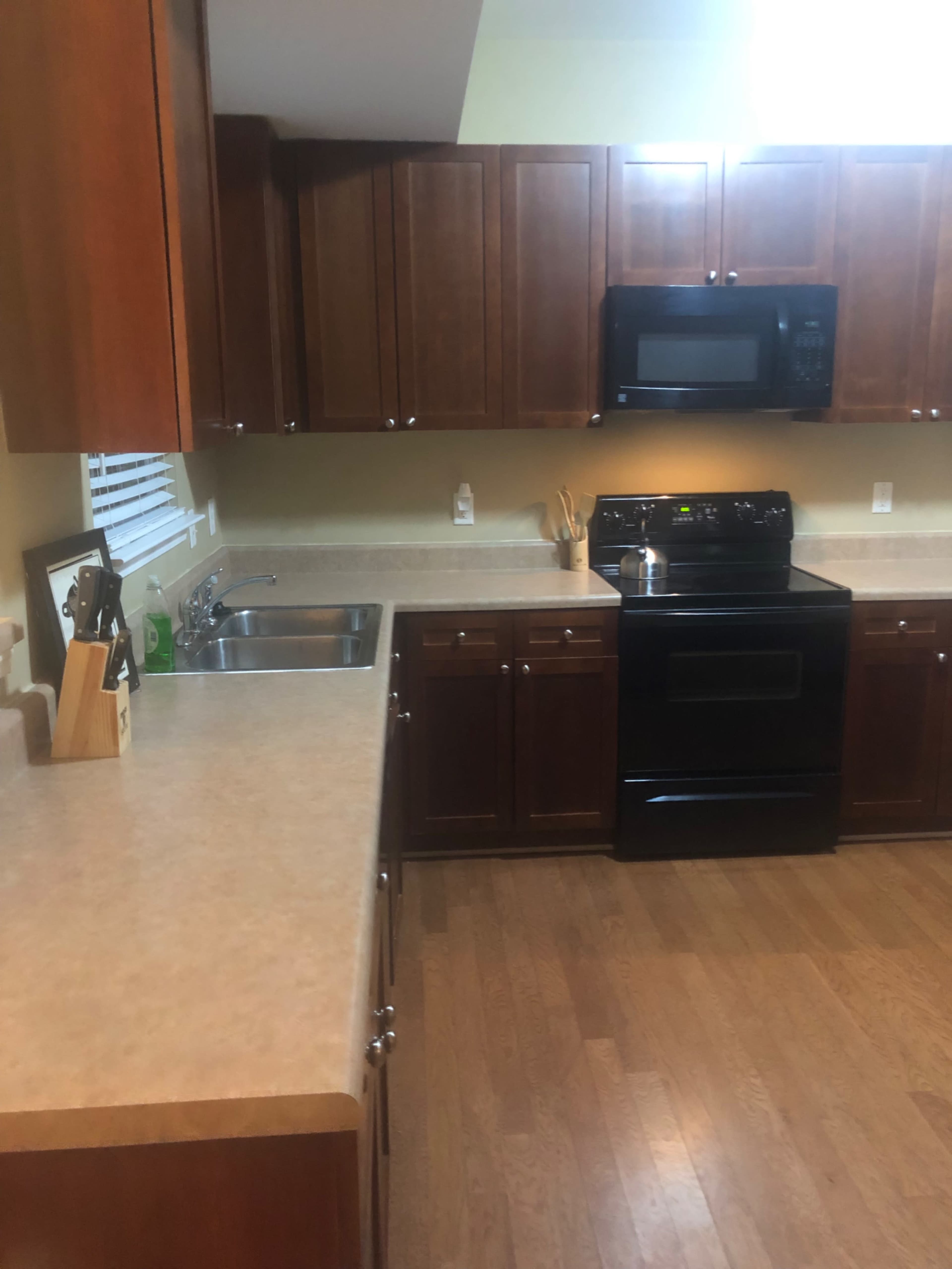 The kitchen features wooden cabinets, a black stove, and a stainless steel sink with a countertop made of beige material.