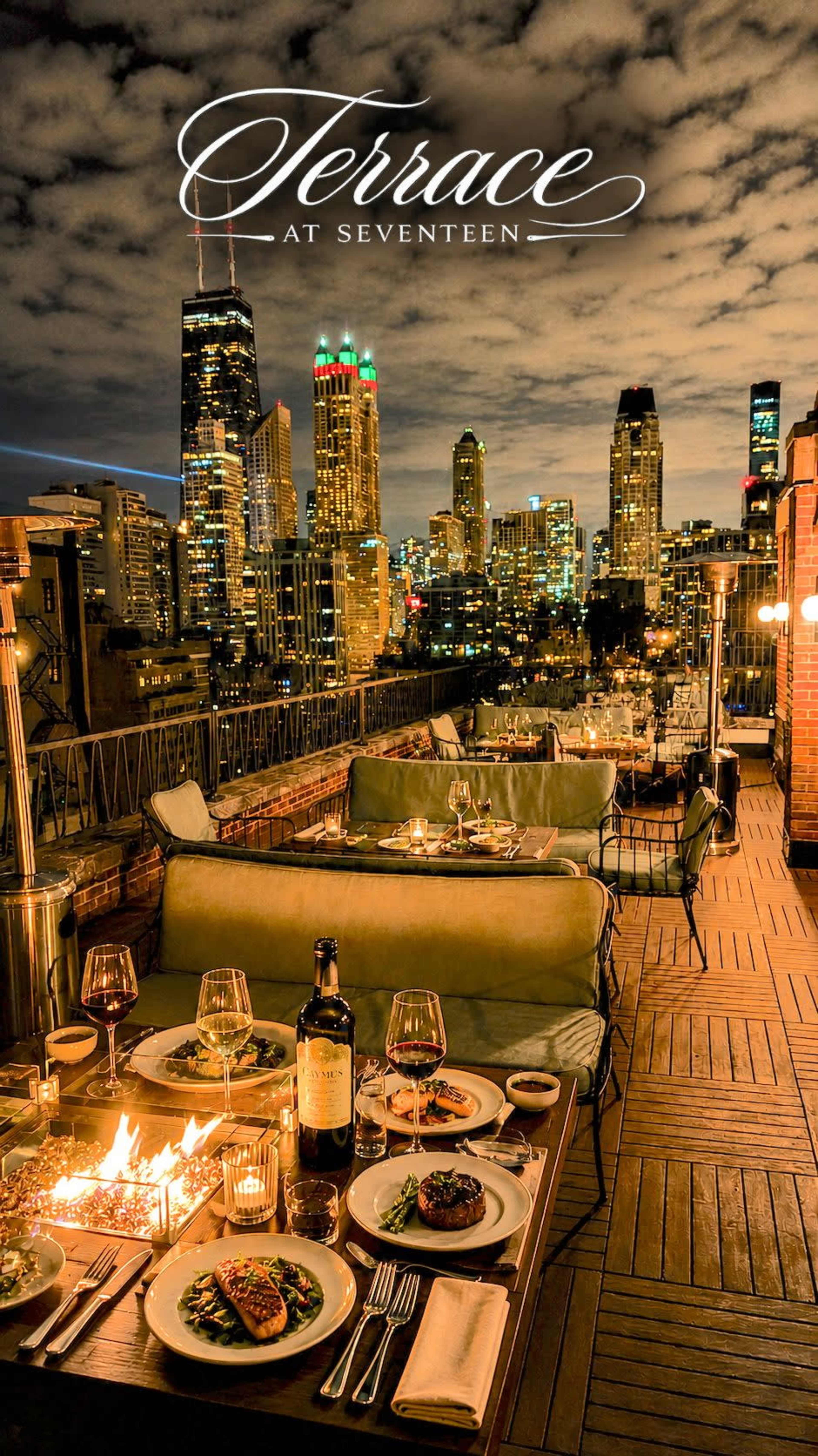 The image shows a rooftop terrace dining area with elegantly set tables overlooking a city skyline illuminated by evening lights.
