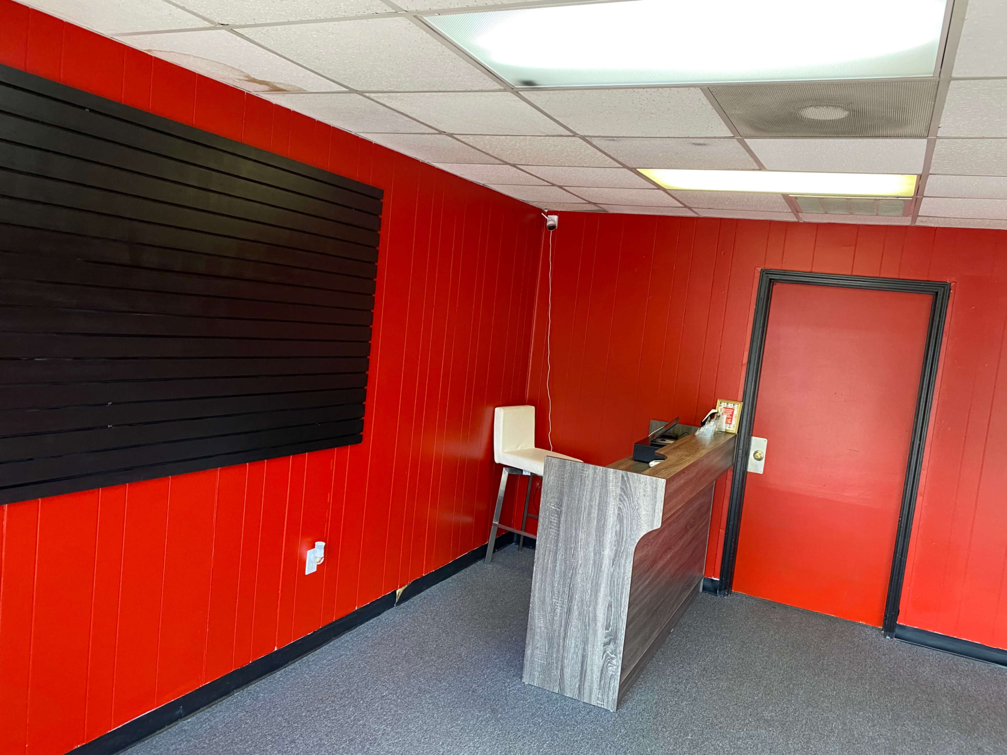 A small interior space with a red wall, a reception counter, a chair, and a door.