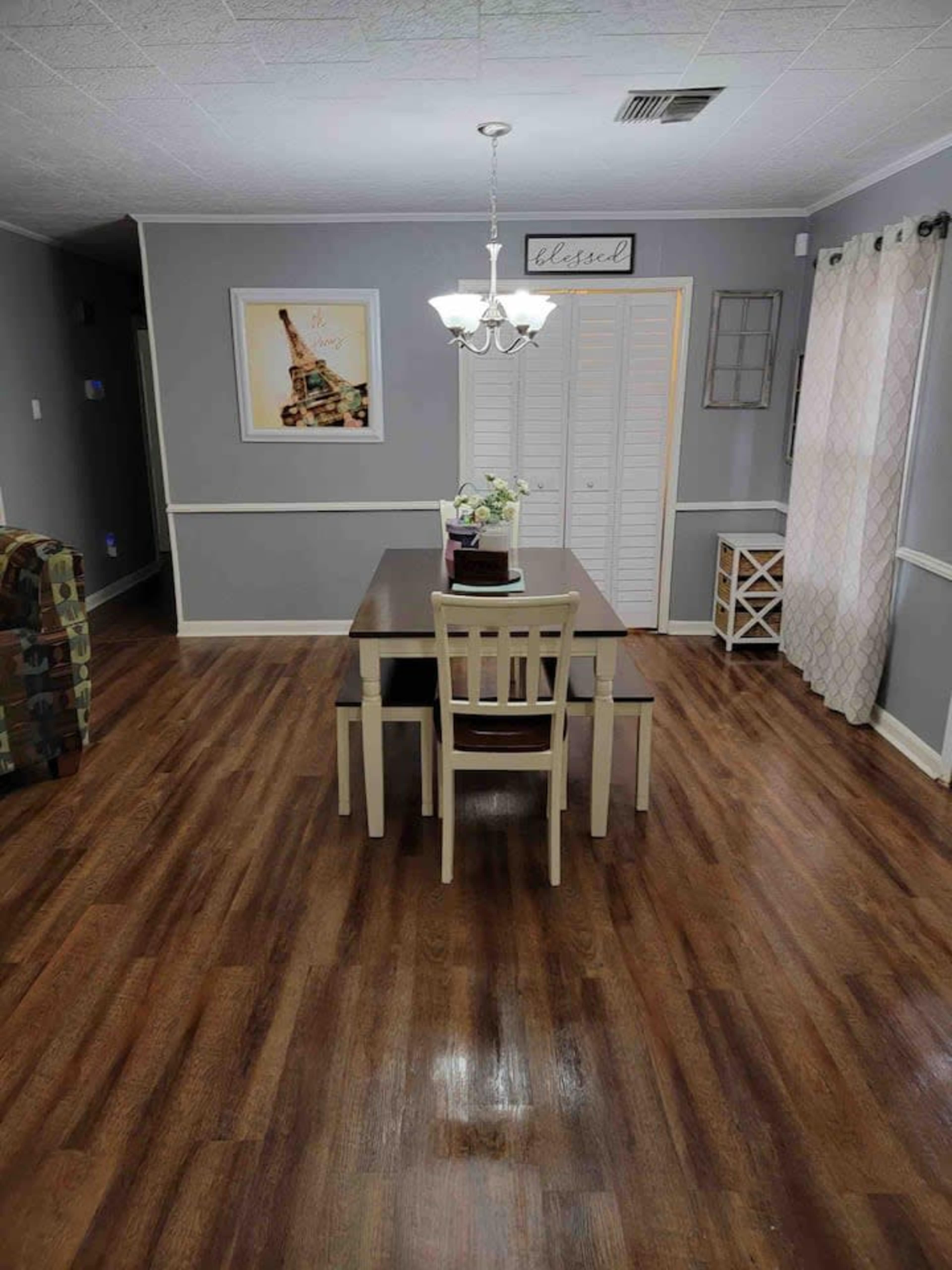 The image shows a dining area with a table and chairs, a chandelier, and a decorative wall.