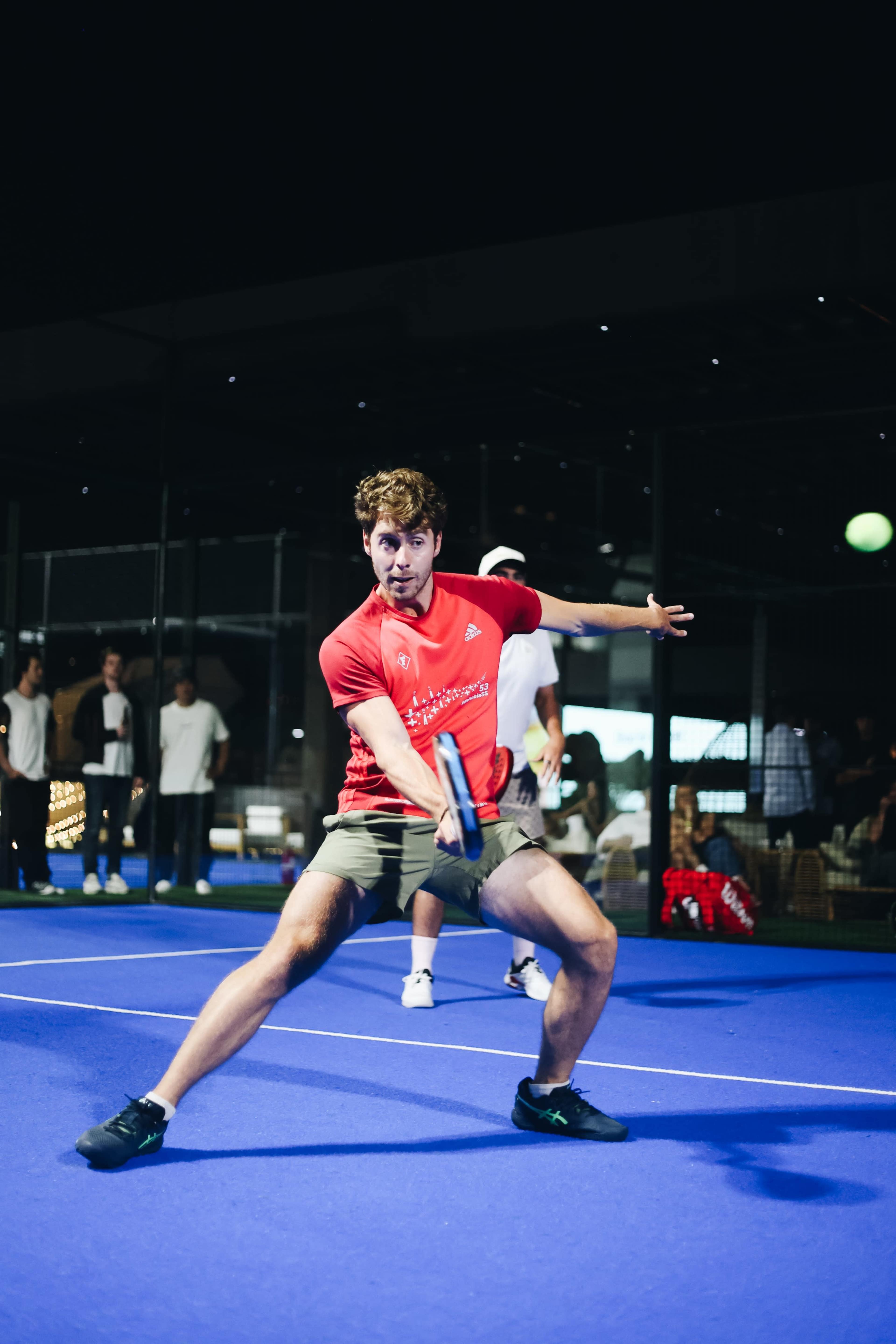 A man in a red shirt is poised to hit a tennis ball on a blue court surrounded by spectators.